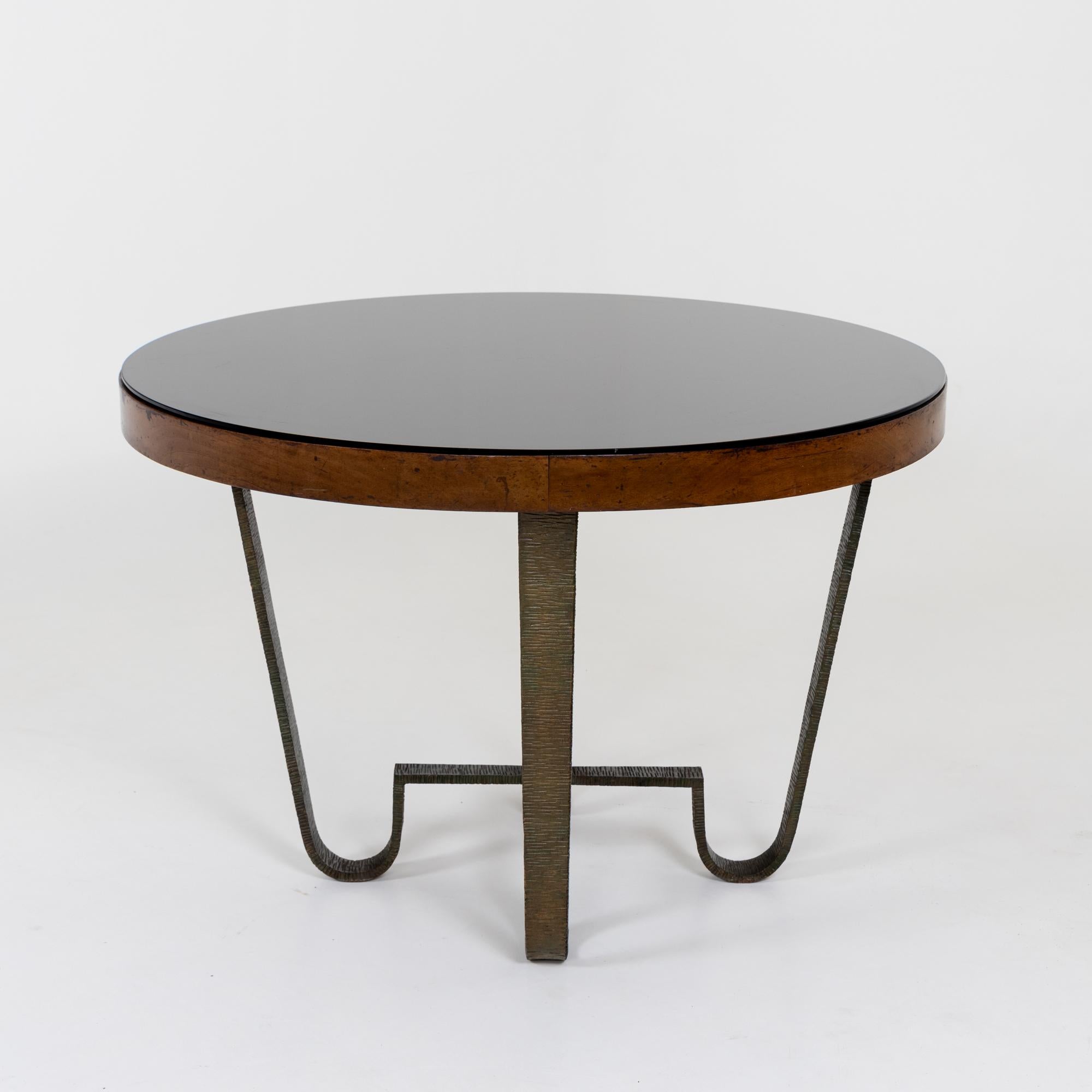 

An Italian Modernist dining table with glass top. 

Highly Textured bronze base of four legs intersecting at the base in a stretcher. The legs support a round wooden top with a black glass surface.

