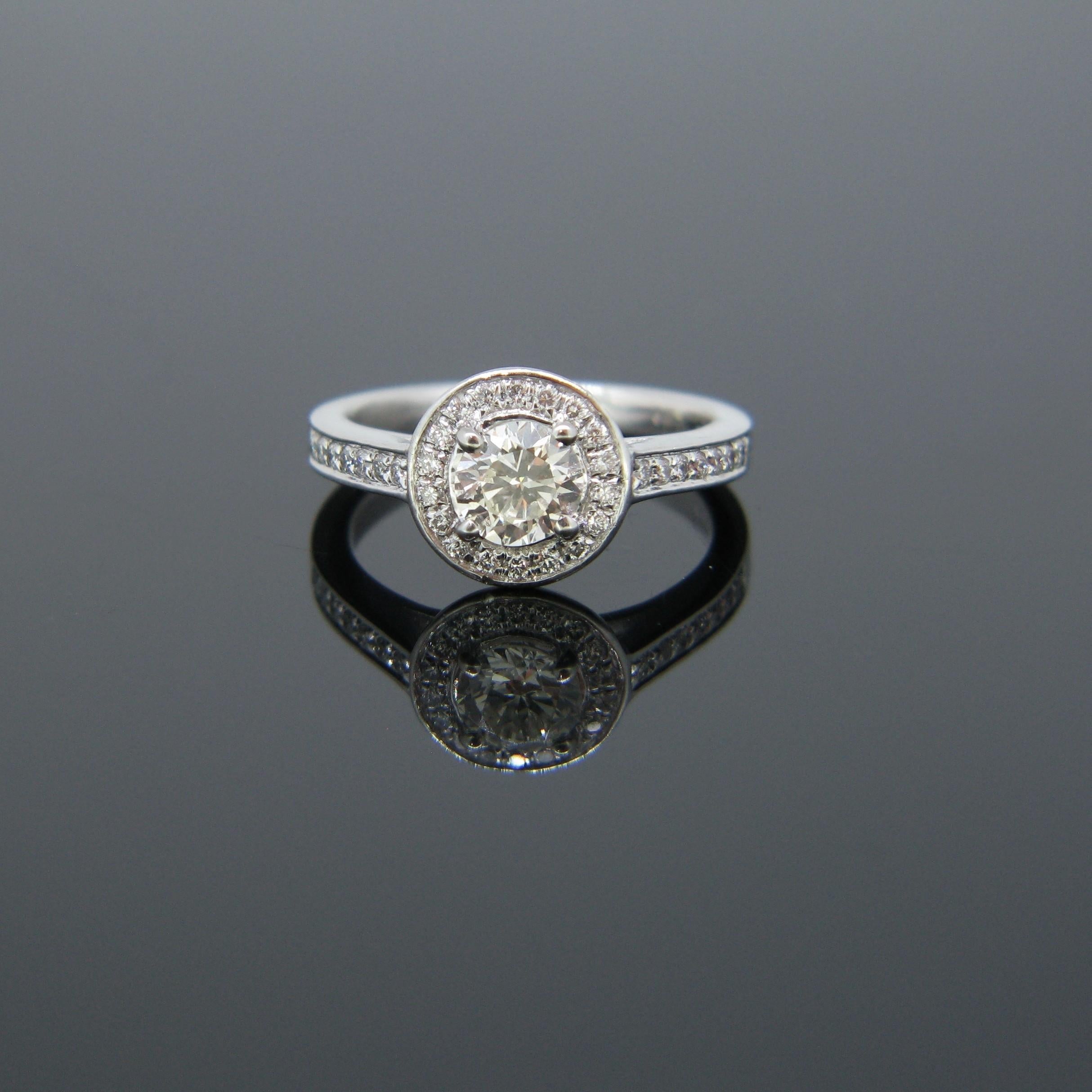This ring is made in platinum. It is set in its centre with a round brilliant cut diamond weighing 0.63ct with colour K and clarity VS1. It is surrounded and adorned on each side with brilliant cut diamonds with a total carat weight of 0.27ct. It is