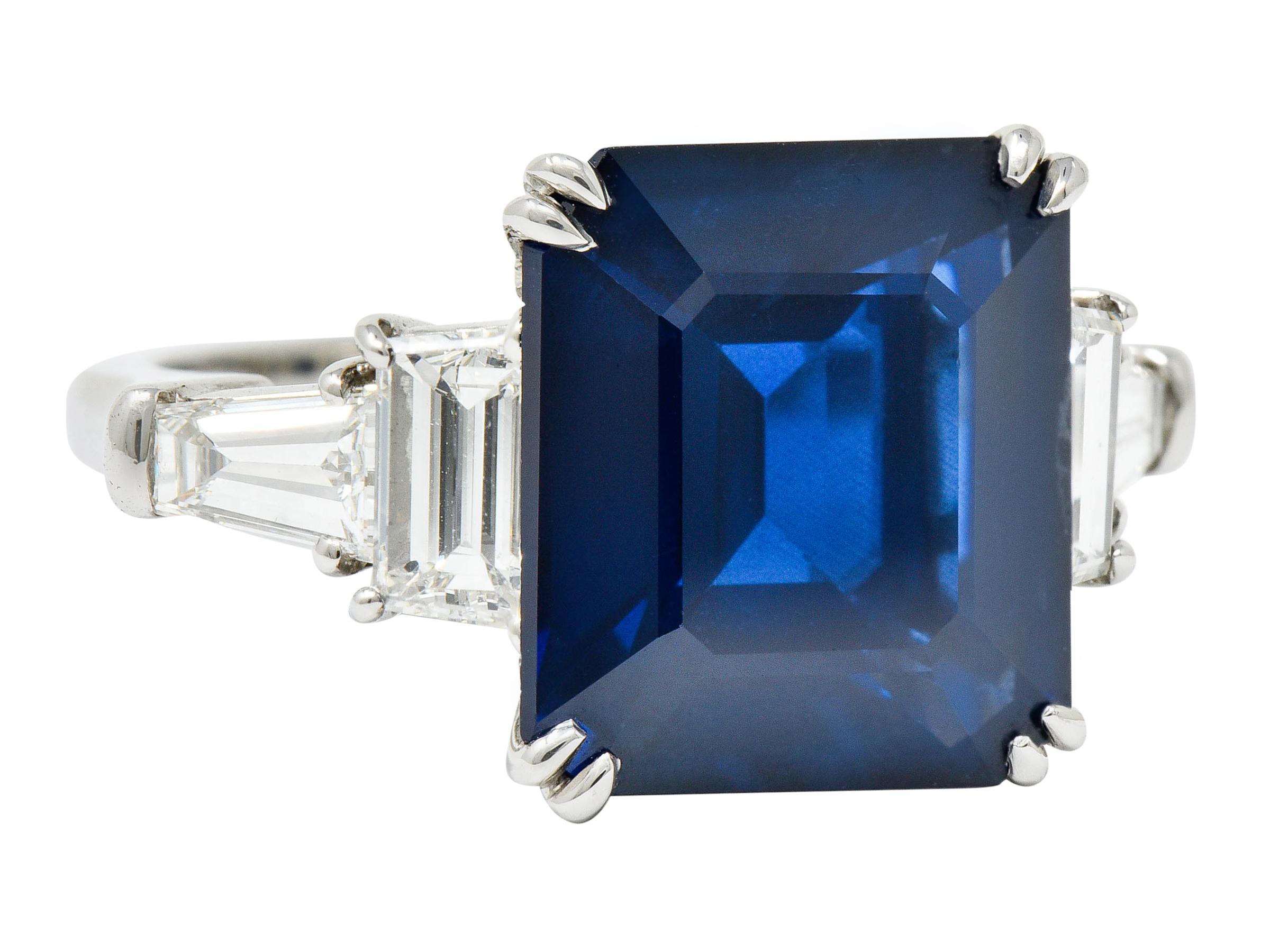 Centering a rectangular step cut sapphire weighing approximately 9.11 carats

Transparent with uniform medium-dark Prussian blue color

Basket and talon set with stylized split prongs, then flanked by tapered and baguette cut diamonds

Weighing in