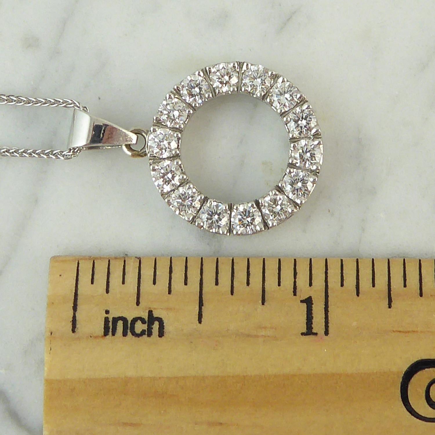 A contemporary diamond pendant in a circular halo design.  Set with 14 round brilliant cut diamonds in white bead claws to an open block style gallery and suspending from a V shaped polished chain runner which is stamped 