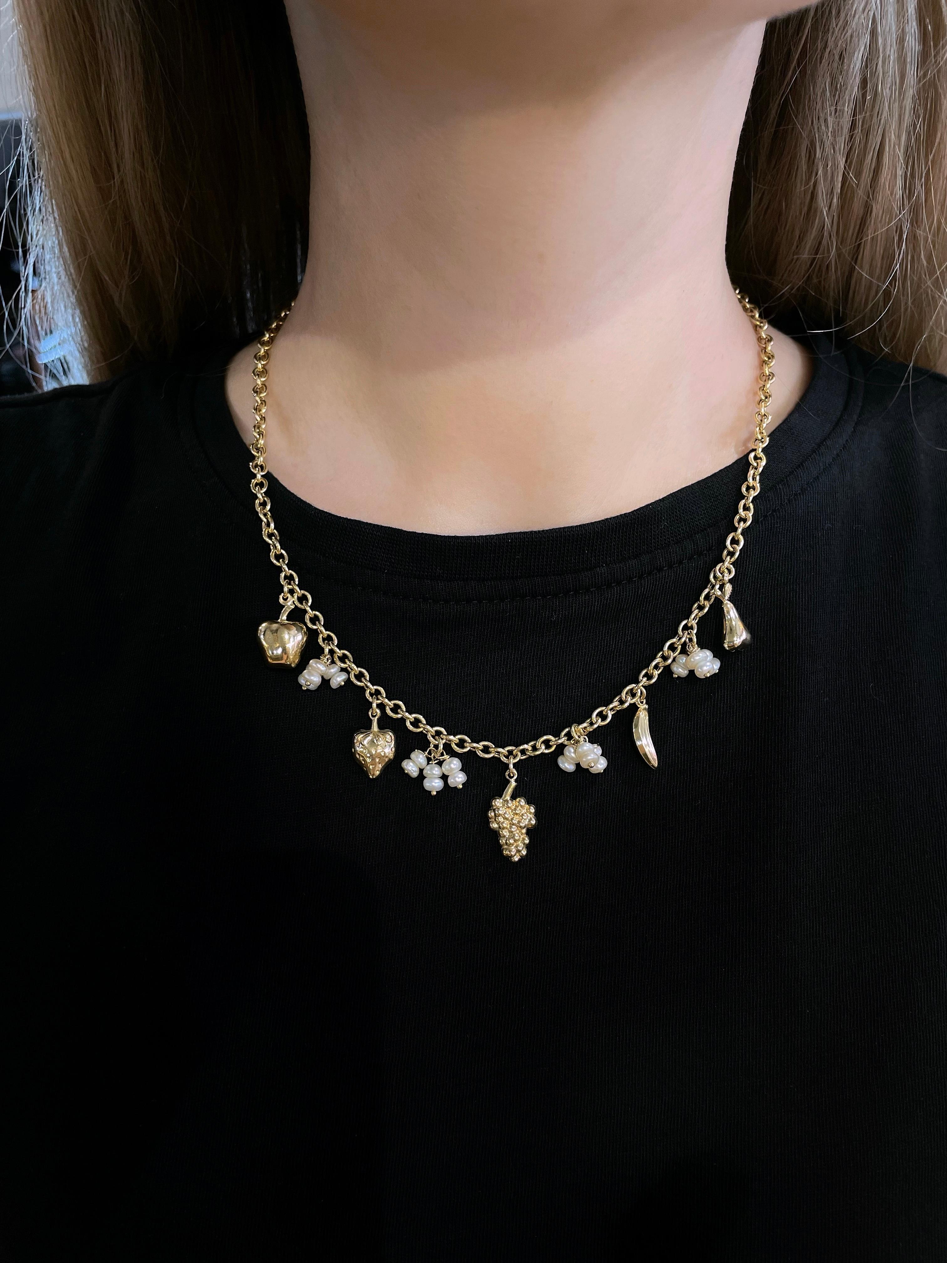 Diese verspielte Kette mit Charme im modernen Design ist aus 18 Karat Gold gefertigt. Das Schmuckstück besteht aus Zuchtperlen und Anhängern in Form von Früchten (Birne, Banane, Weintraube, Erdbeere, Apfel). Um 2000. 

Signiert mit 