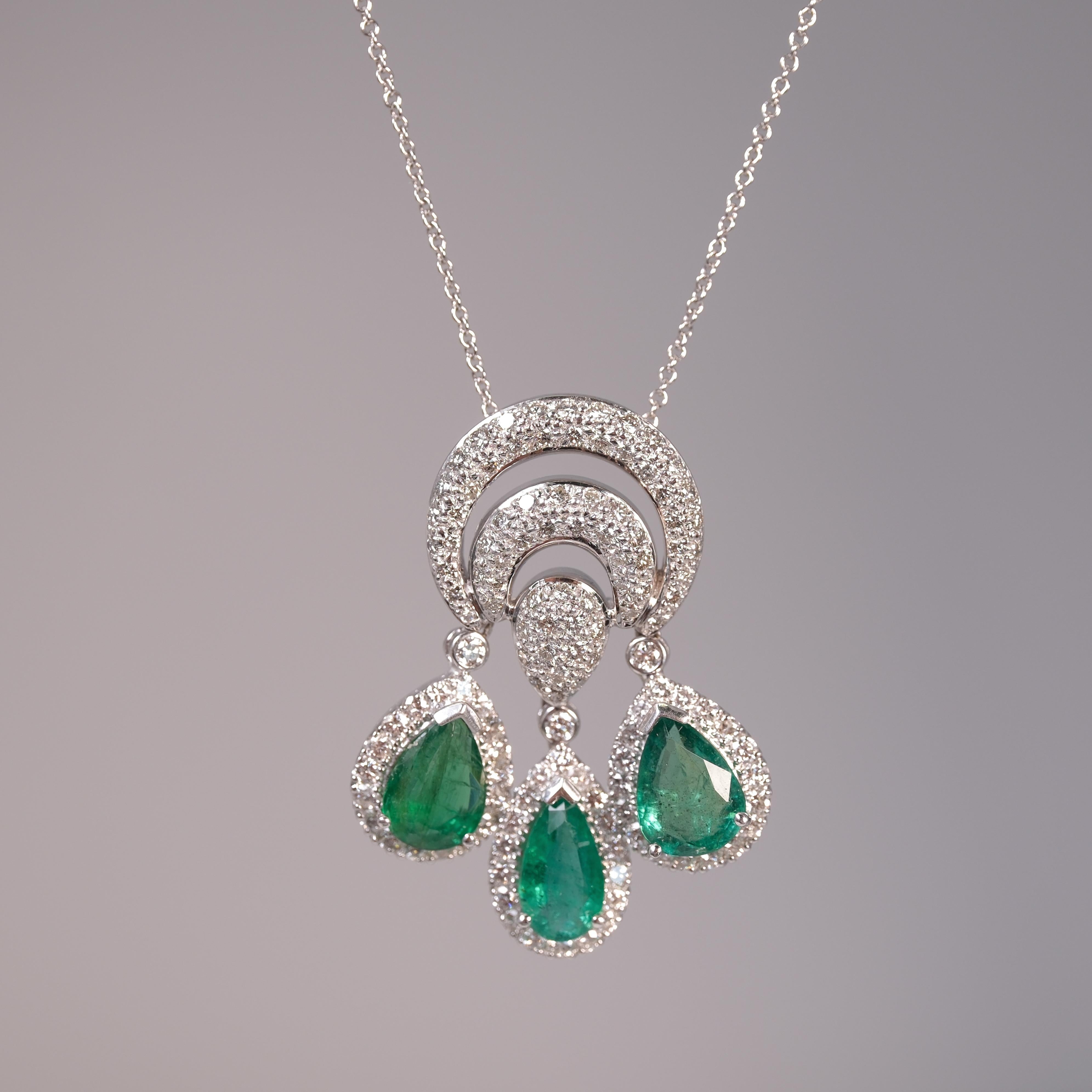 Crafted from 18 karat white gold, this pendant showcases three richly-hued pear cut emeralds, framed by approximately 1.75 carats of round diamonds. A delicate 14 karat chain complements the striking centerpiece, merging elegance with profound