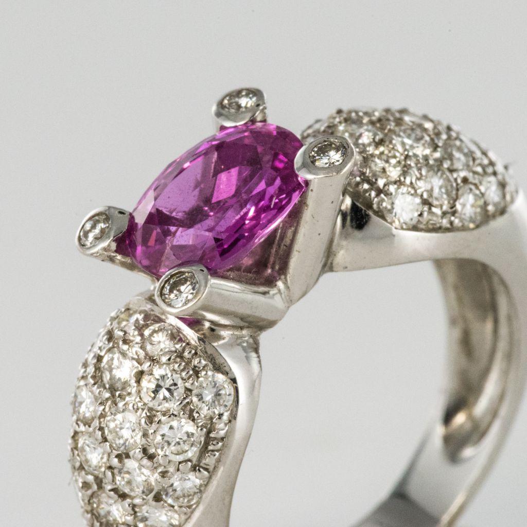 Ring in 18 karat white gold, eagle head hallmark. 
Featuring a claw set oval pink sapphire at the front with diamond pave at each side; the claws that hold the sapphire are each set with a diamond. 
Total weight of sapphire : 1.88 carats