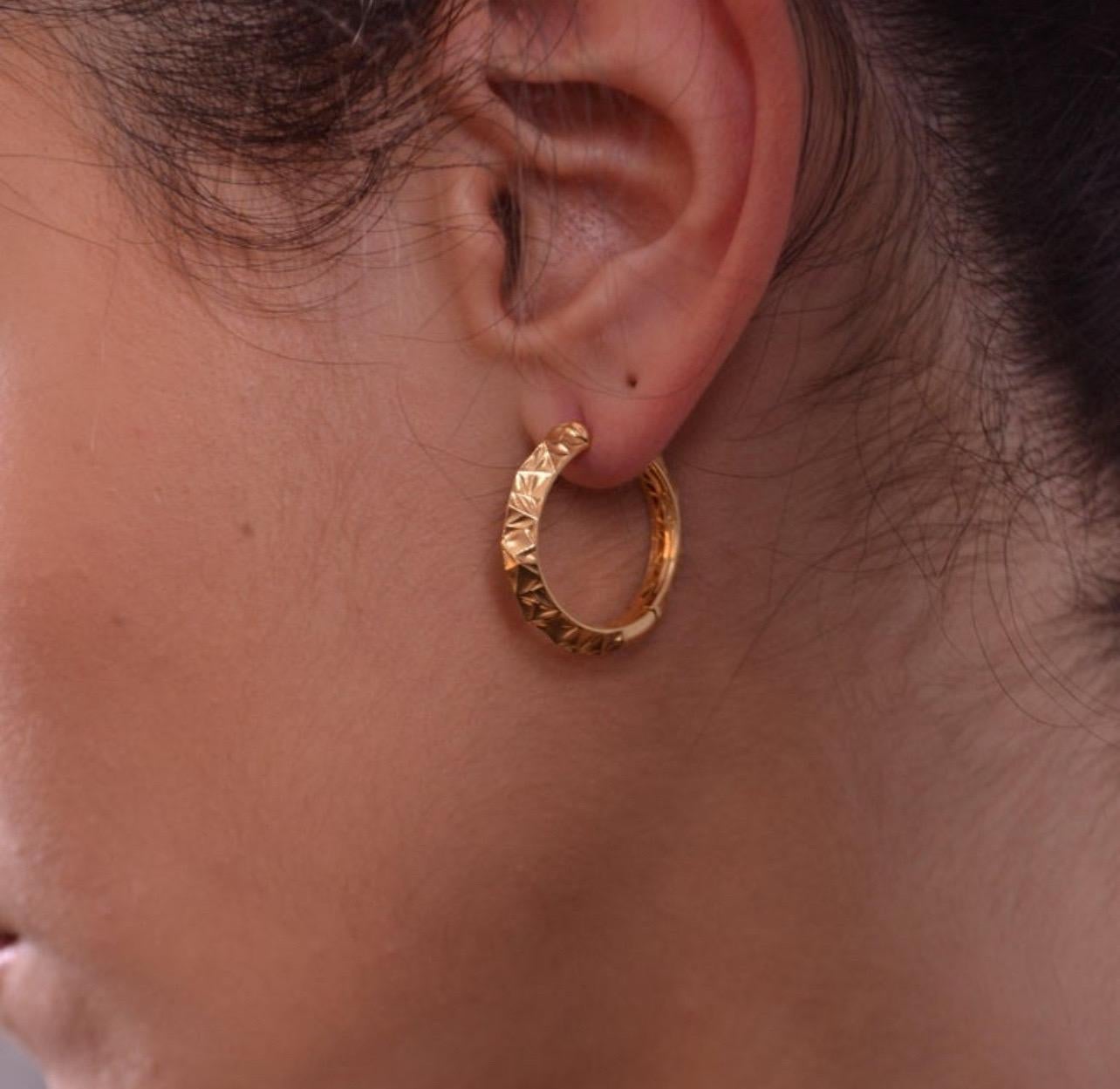 These elegant hoop earrings are crafted from 18K yellow gold and feature a distinctive textured design that adds depth and dimension. The subtle geometric pattern etched into the gold creates a unique visual effect, making these hoops stand out