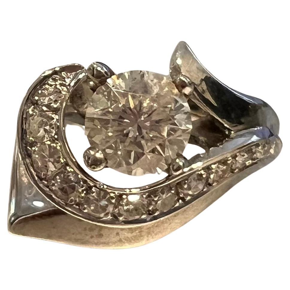 A graceful diamond ring centering a round brilliant diamond of H color, SI1 clarity weighing approximately 1.50 carats, accented by a swirl of sparkling round diamonds in a sculptural 14 karat white gold mounting. The diamond swirl is composed of