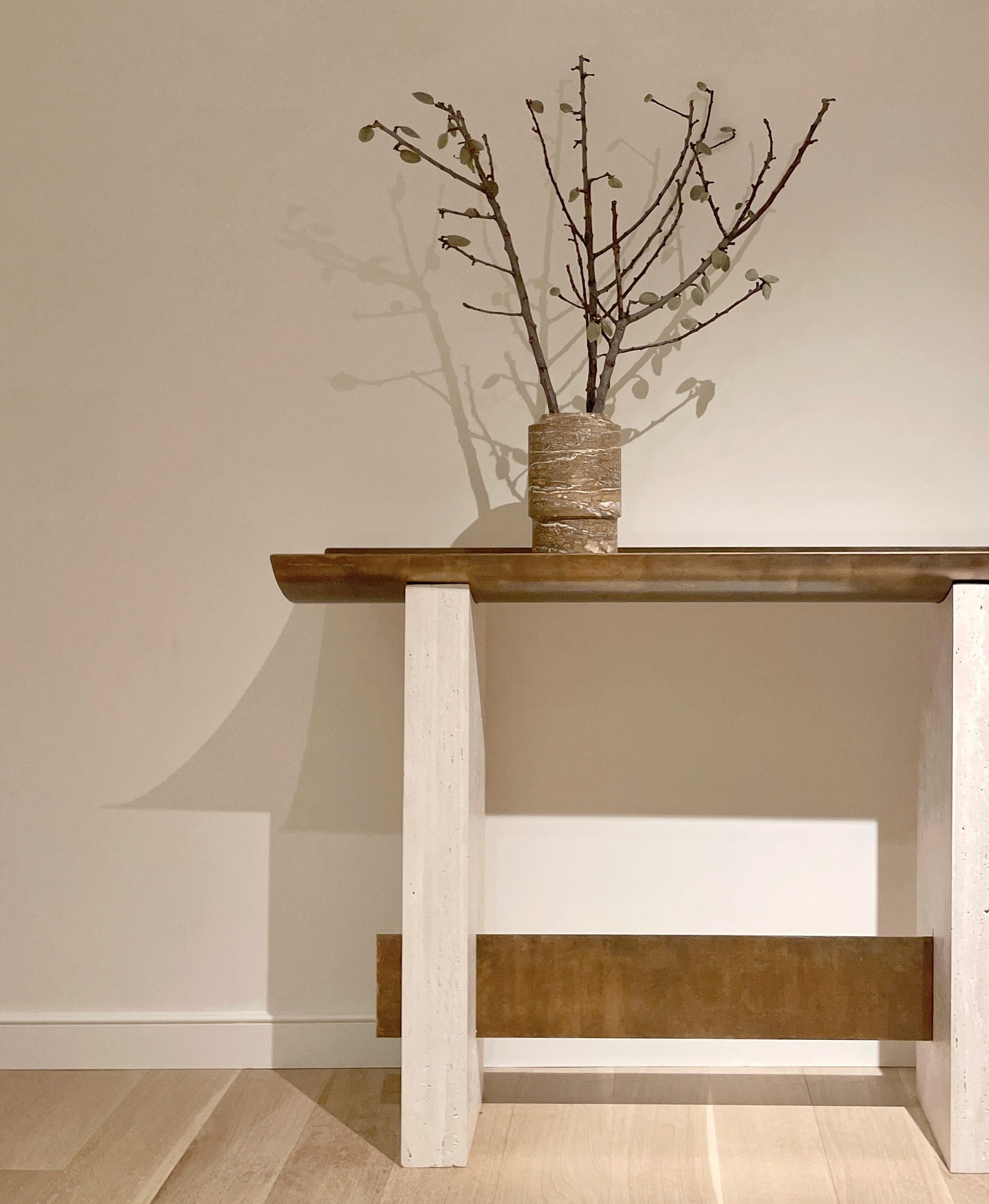 Console with unfilled travertine legs and patinated brass top detailing.
Brut has a travertine piece and a brass stick on the top for accessories, envelops or personal treasures.

Brass patina was applied to the Brut Console by designer to create