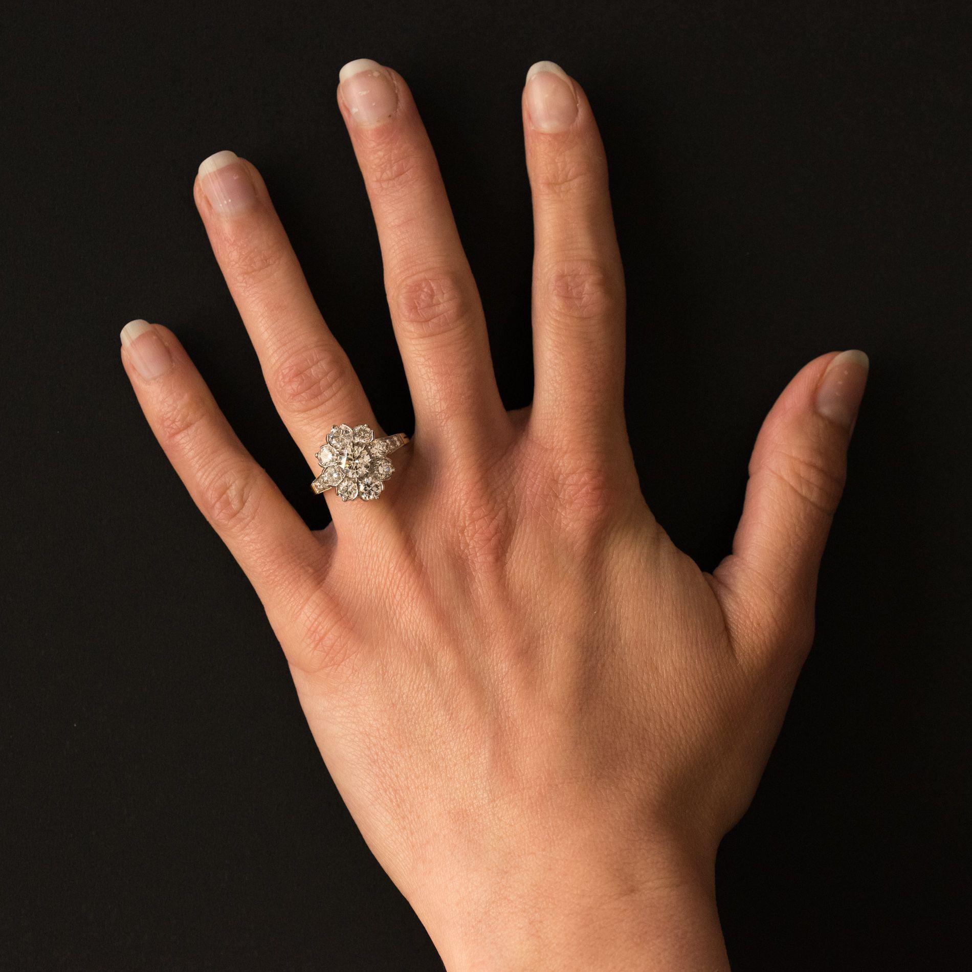 Ring in 18 karat yellow gold, eagle head hallmark and platinum, dog head hallmark.
In the shape of a daisy ring, it is set in the center with 8 claws of a brilliant-cut diamond surrounded by 8 diamonds set half-moon. On either side of the ring, 2