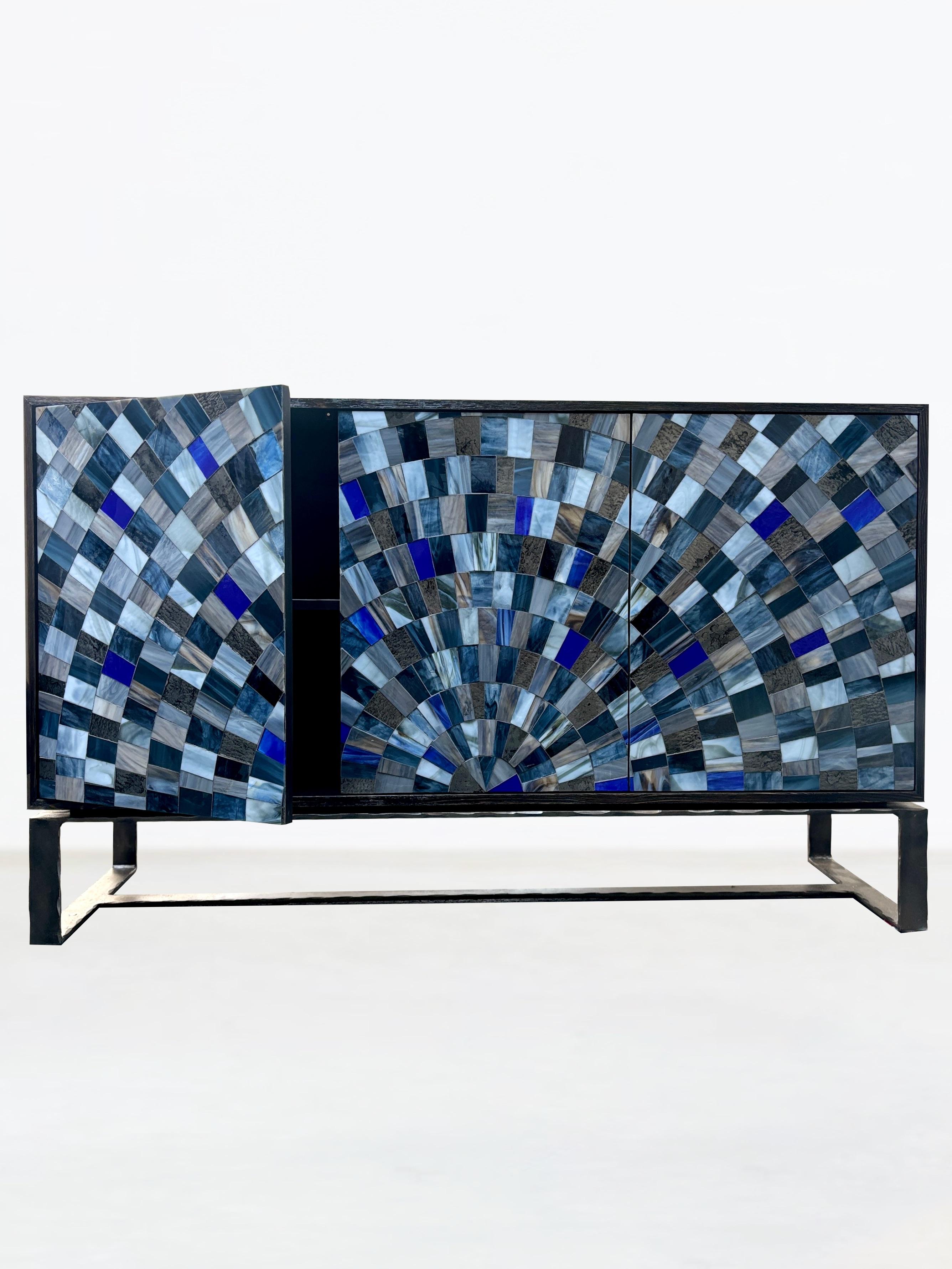 Il Modern Color 3-Door Sunburst Mosaic Buffet di Ercole Home è dotato di 3 ante con chiusura a sfioramento e mosaico di vetro tagliato a mano con motivo Sunburst nei colori Dark London Gray, Antique Pewter, Cloudy Notte e Cobalt. Cassa in legno di