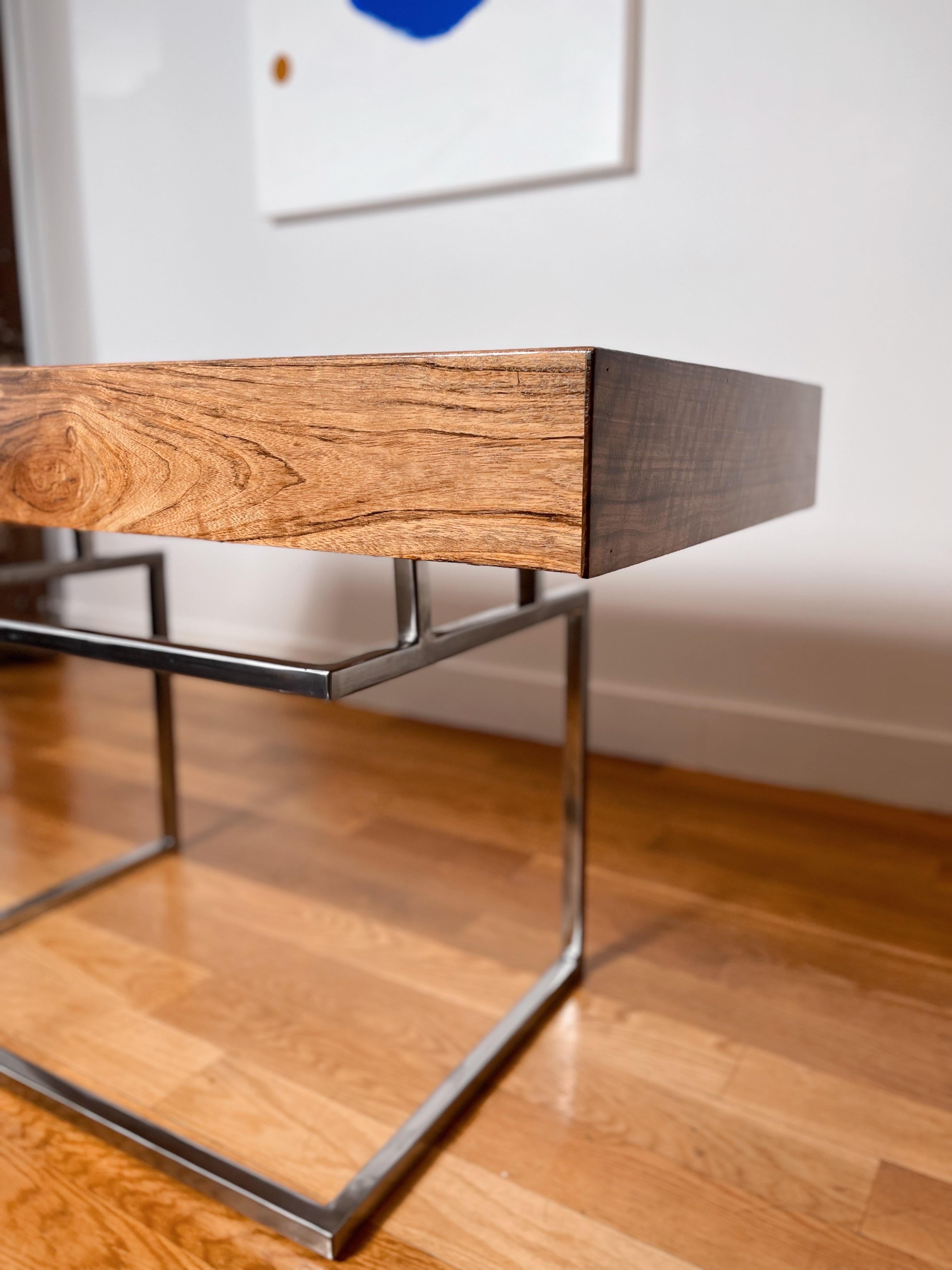 This desk is comprised of exotic Shedua hardwood and a solid hand polished stainless steel base. The three equal sized drawers provide plenty of storage for pens, small electronics and papers/documents. The beveled edge drawer fronts are reminiscent