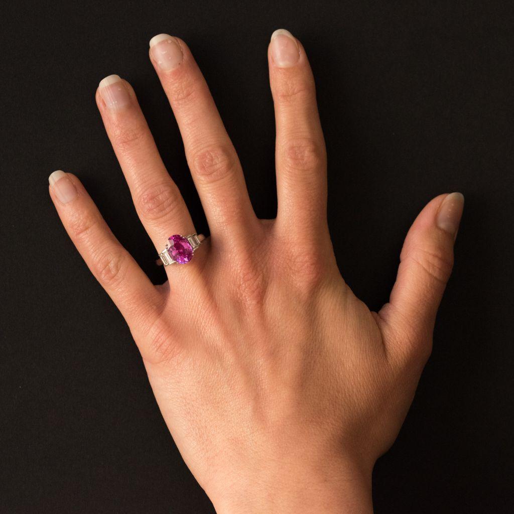 Ring in 18 karat white gold, eagle head hallmark. 
This ring features a 4 double claw set oval bright pink sapphire, accentuated at both sides with 2 baguette diamonds. 
Total weight of sapphire: 3.55 carats approximately, 
Total diamond weight: