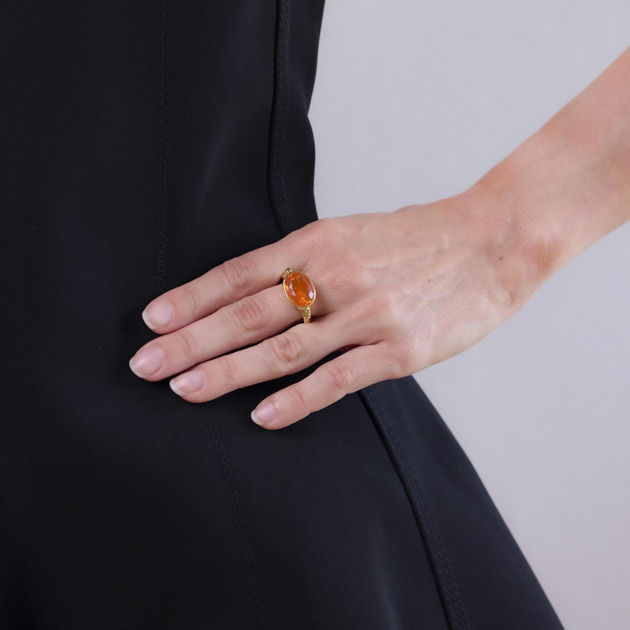 This modern ring from the 2010s is crafted in 18k yellow gold and features a vivid oval cut fire opal weighing approximately 3.90 carats. The setting highlights the opal’s intense orange hue with warm gold tones. Hallmarked with a purity stamp, this
