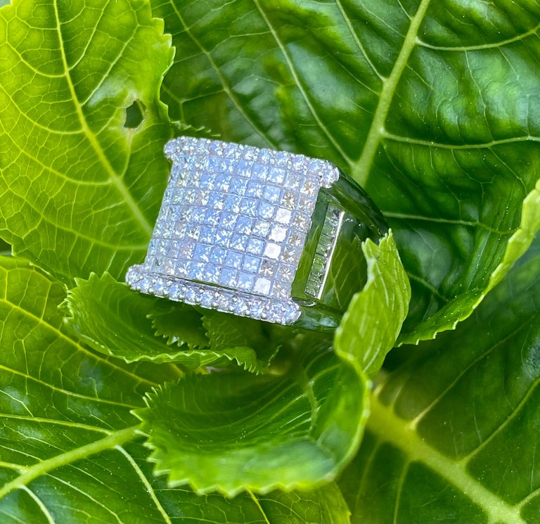 Heavy 18 karat white gold modern design unisex ring features invisibly set princess cut diamonds on the top of the ring, prong set round brilliant diamonds on each side of the top of the ring, and inlaid invisibly set baguette diamonds in sections