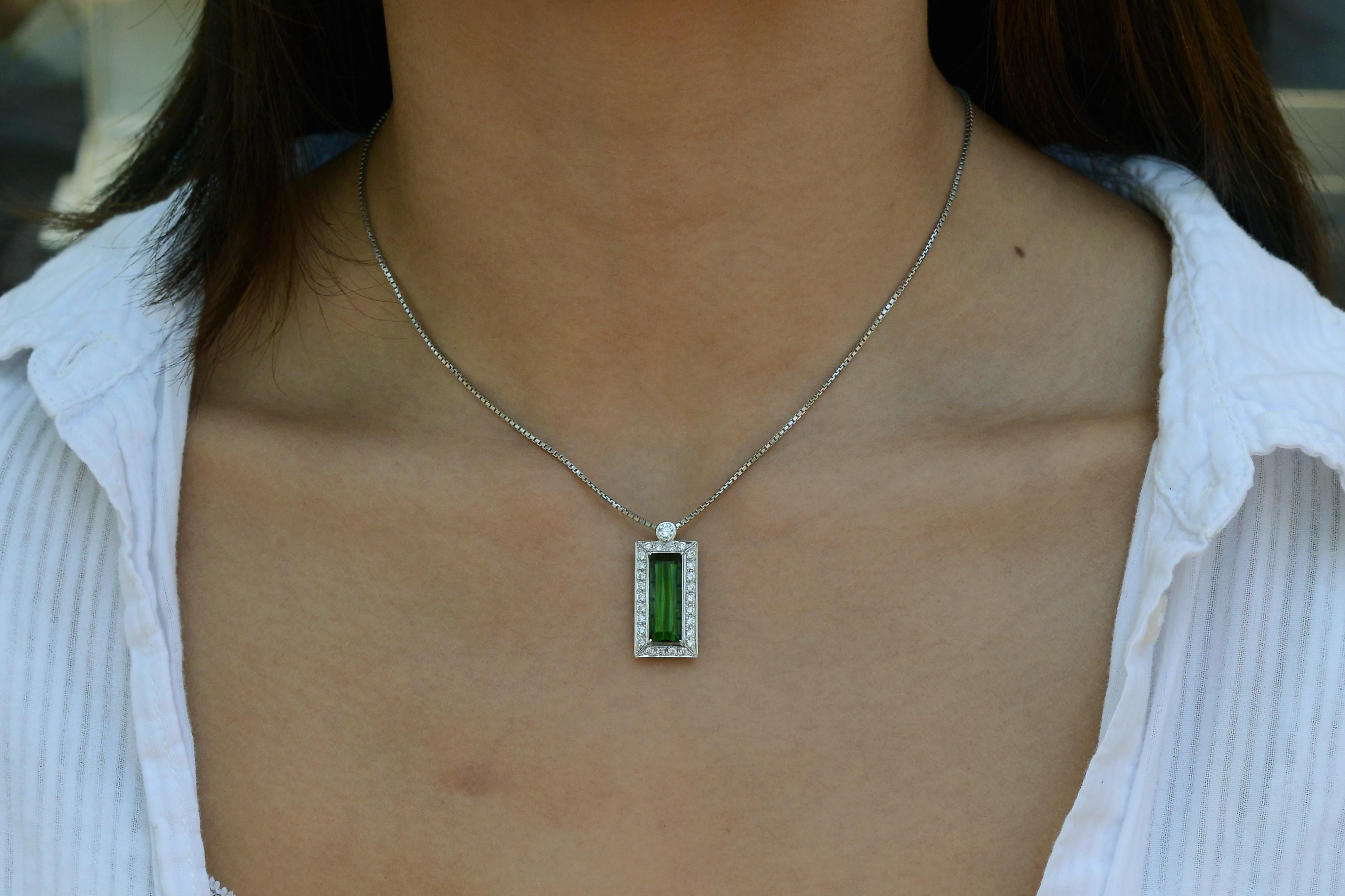 A modern design pendant presenting a towering tourmaline weighing nearly 6 carats. The stunning, vivid grass-green natural gemstone and 27 round brilliant diamonds are precisely prong set in platinum, all suspended from a solid box chain. A lovely