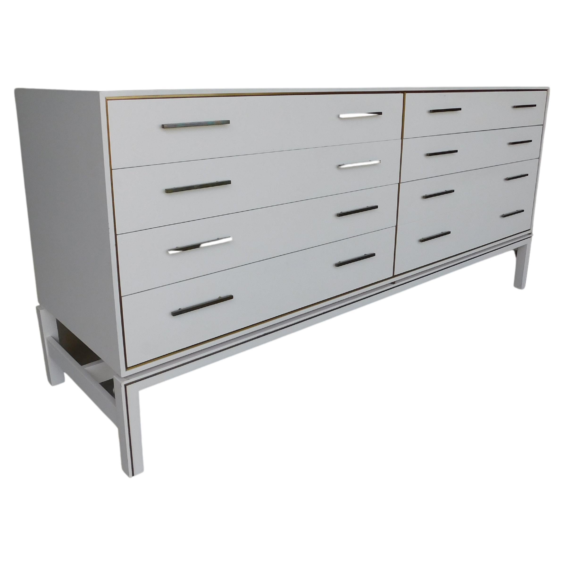 Features - 7 dovetailed drawers, mounted with brass pulls, and framed border in brass surrounding, Resting up on stretcher style base trimmed in brass accent. Factory original powder white paint finish adding to the clean straight decorative lines.