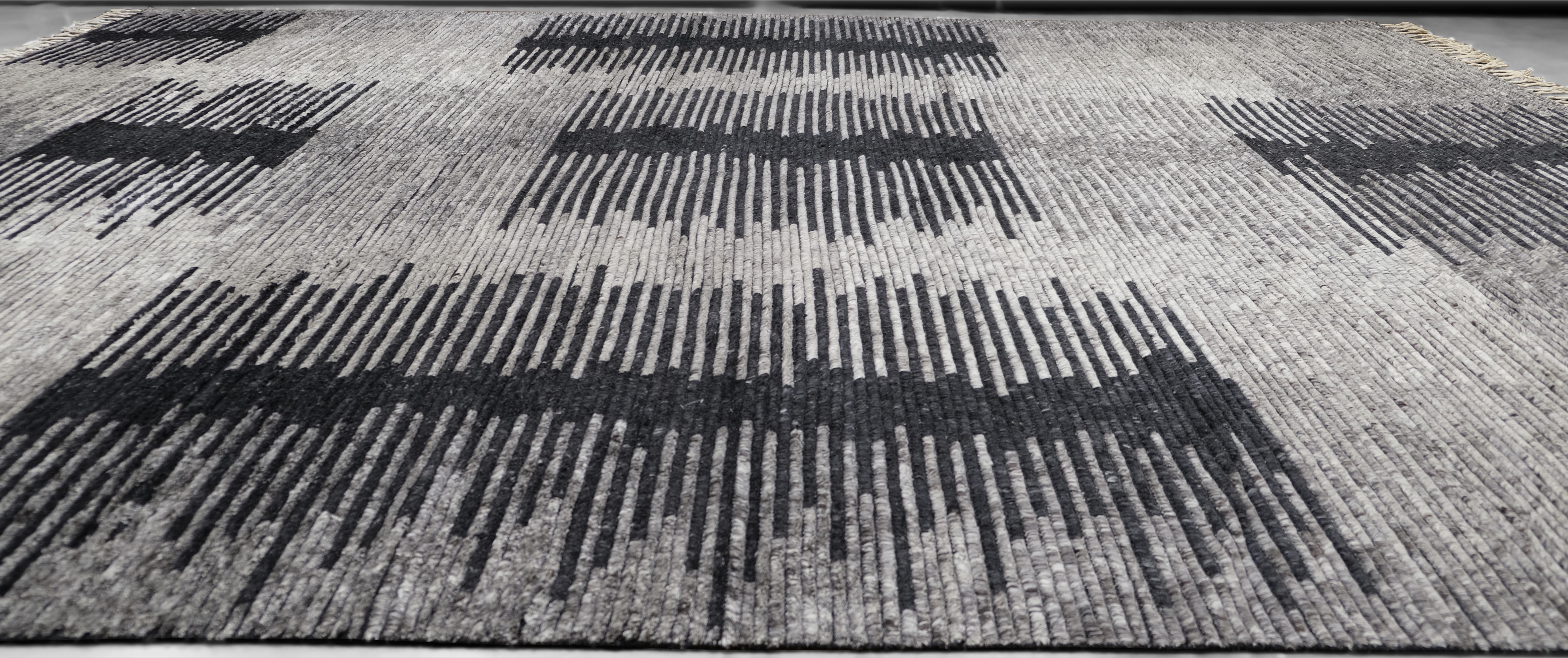 Dieser handgeknüpfte Wollteppich zeichnet sich durch ein auffälliges geometrisches Muster in Schwarz und Grau aus, das einen auffälligen visuellen Kontrast bildet. Das geradlinige Design mit unregelmäßigen Formationen von Streifen verleiht ihm einen