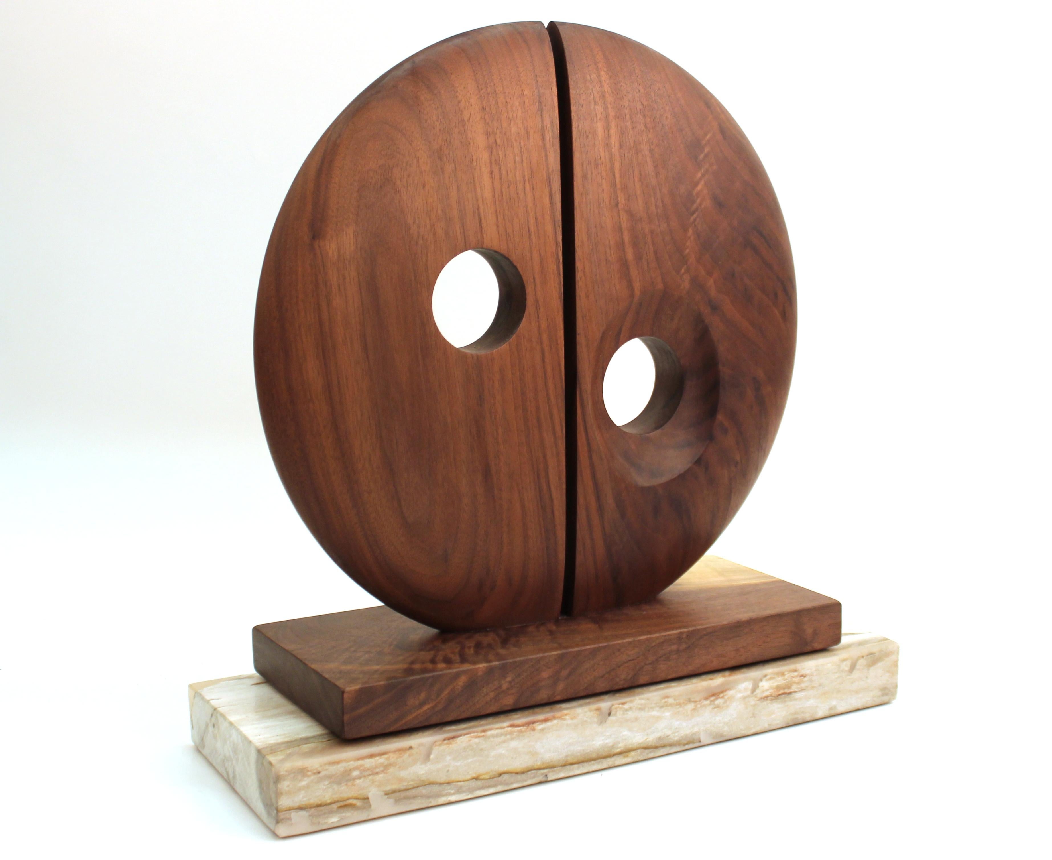 Modern abstract tabletop sculpture in carved wood, composed of a large bisected disc with circular openings. The sculpture is fixed atop a wooden base resting on a stone base. In great vintage condition with age-appropriate wear and use.