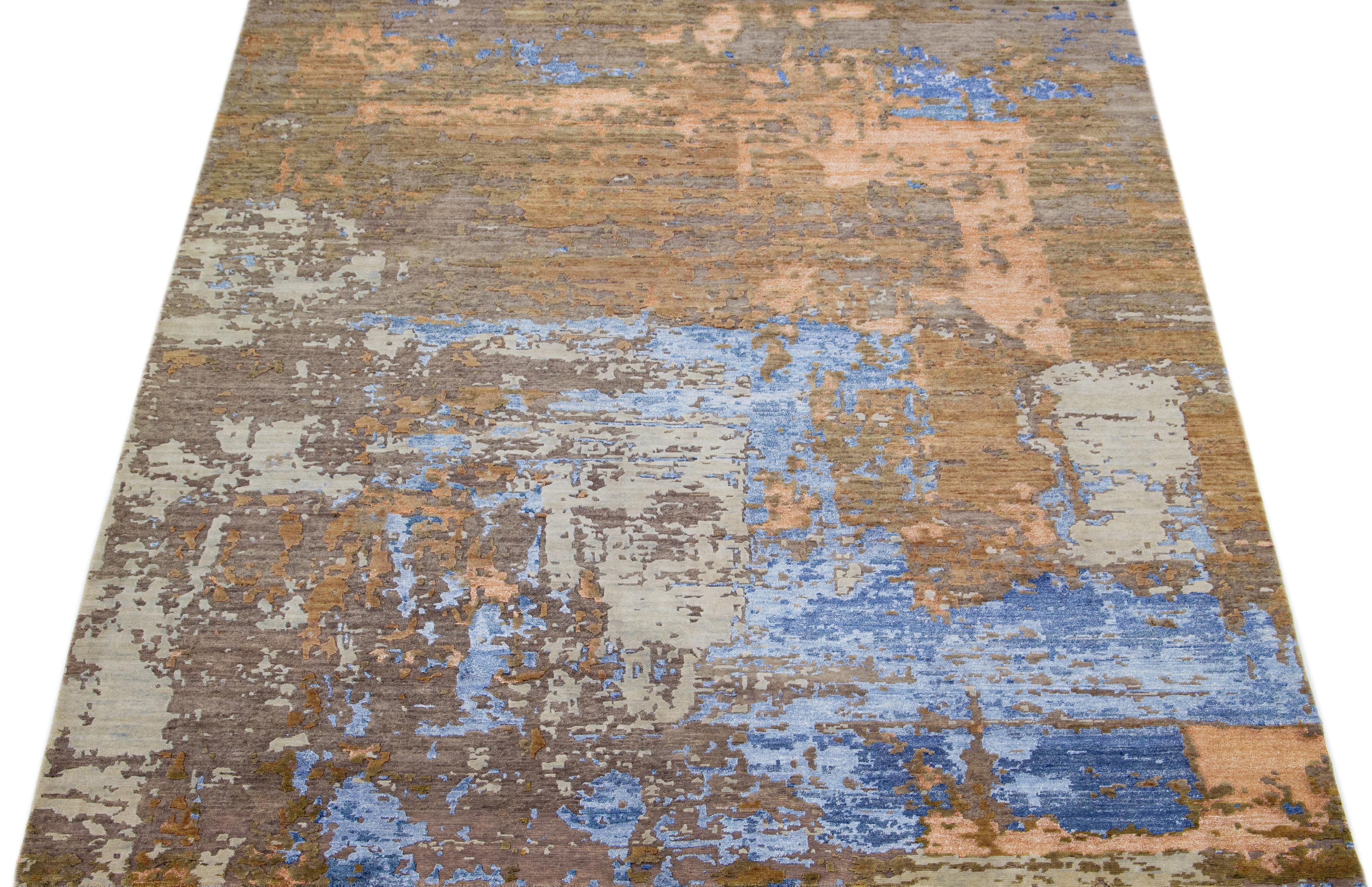 Ce tapis indien en laine et soie mélangées présente un champ brun avec un motif abstrait détaillant des couleurs orange et bleues. Ses matériaux composés lui confèrent robustesse et longévité, tandis que son design ornemental insuffle de la