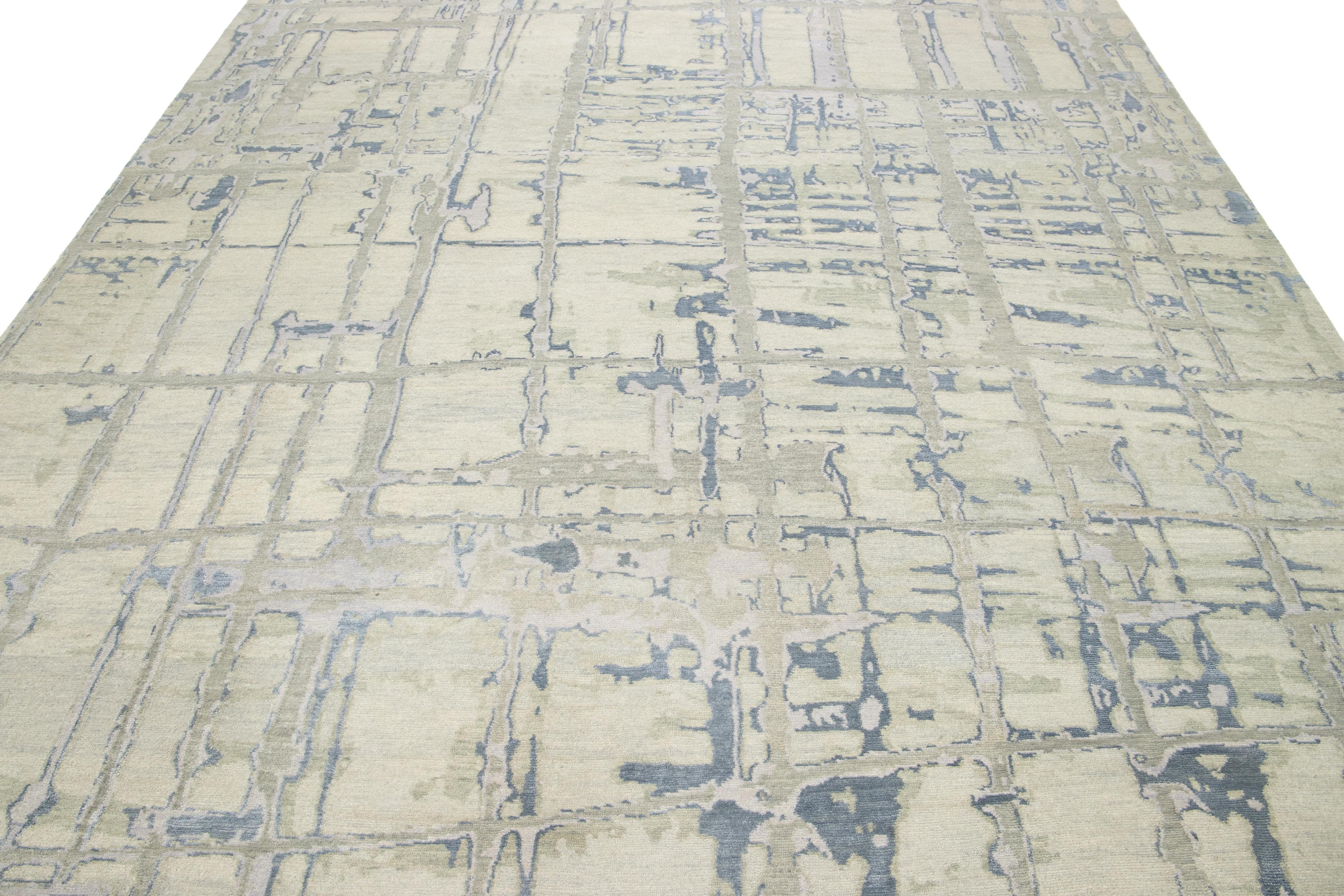 Dieser moderne Teppich aus tibetischer Wolle hat ein hellgraues und beiges Feld mit blauen und silbernen Akzenten in dem abstrakten Design. 

Dieser Teppich misst 9' x 12'.
