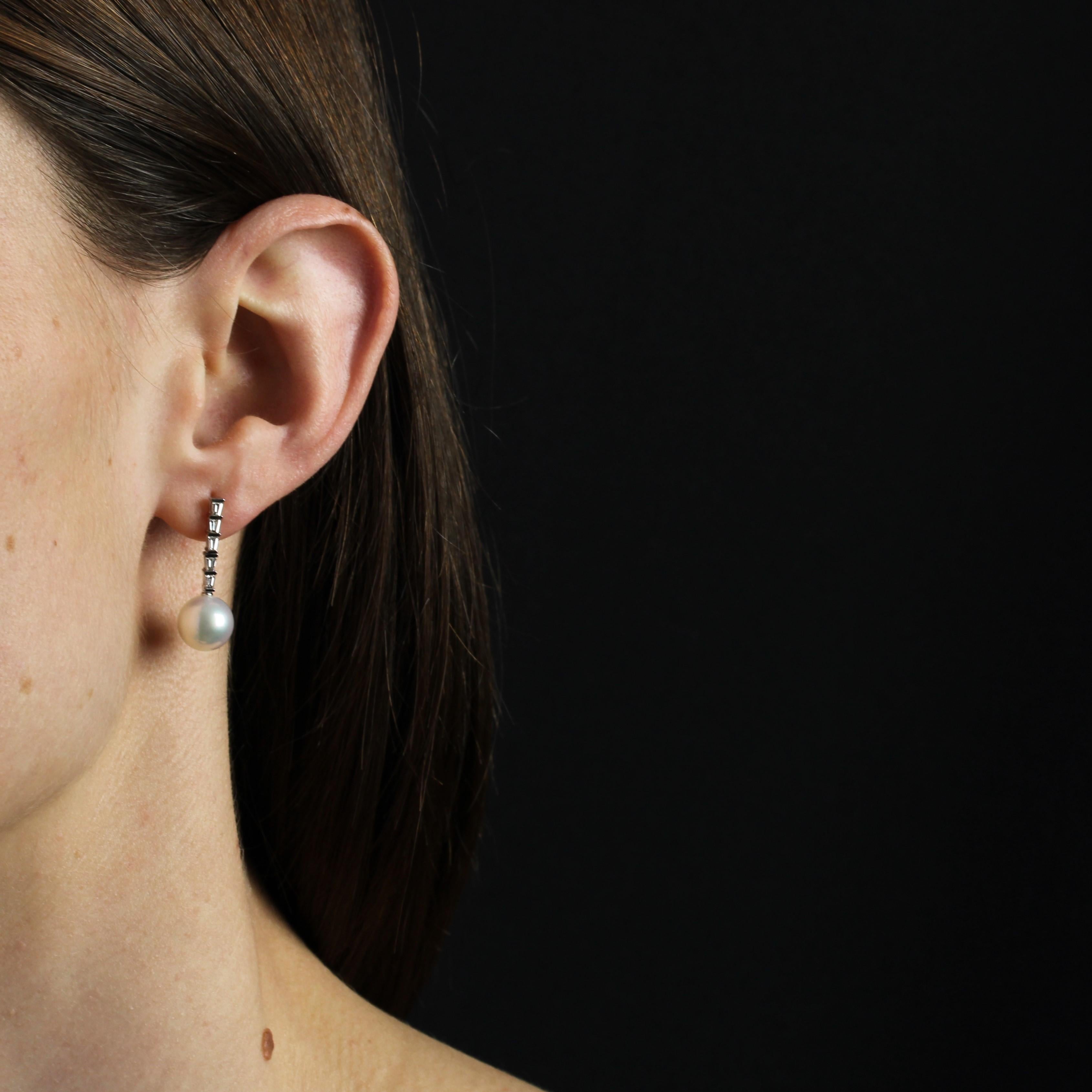 Für gepiercte Ohren.
Ohrringe aus 18 Karat Weißgold.
Diese baumelnden Ohrringe im Art-déco-Stil sind mit einer Reihe von 5 Diamanten im Prinzessinnenschliff besetzt, die eine runde, perlweiße Akoya-Zuchtperle halten. Das Verschlusssystem besteht aus