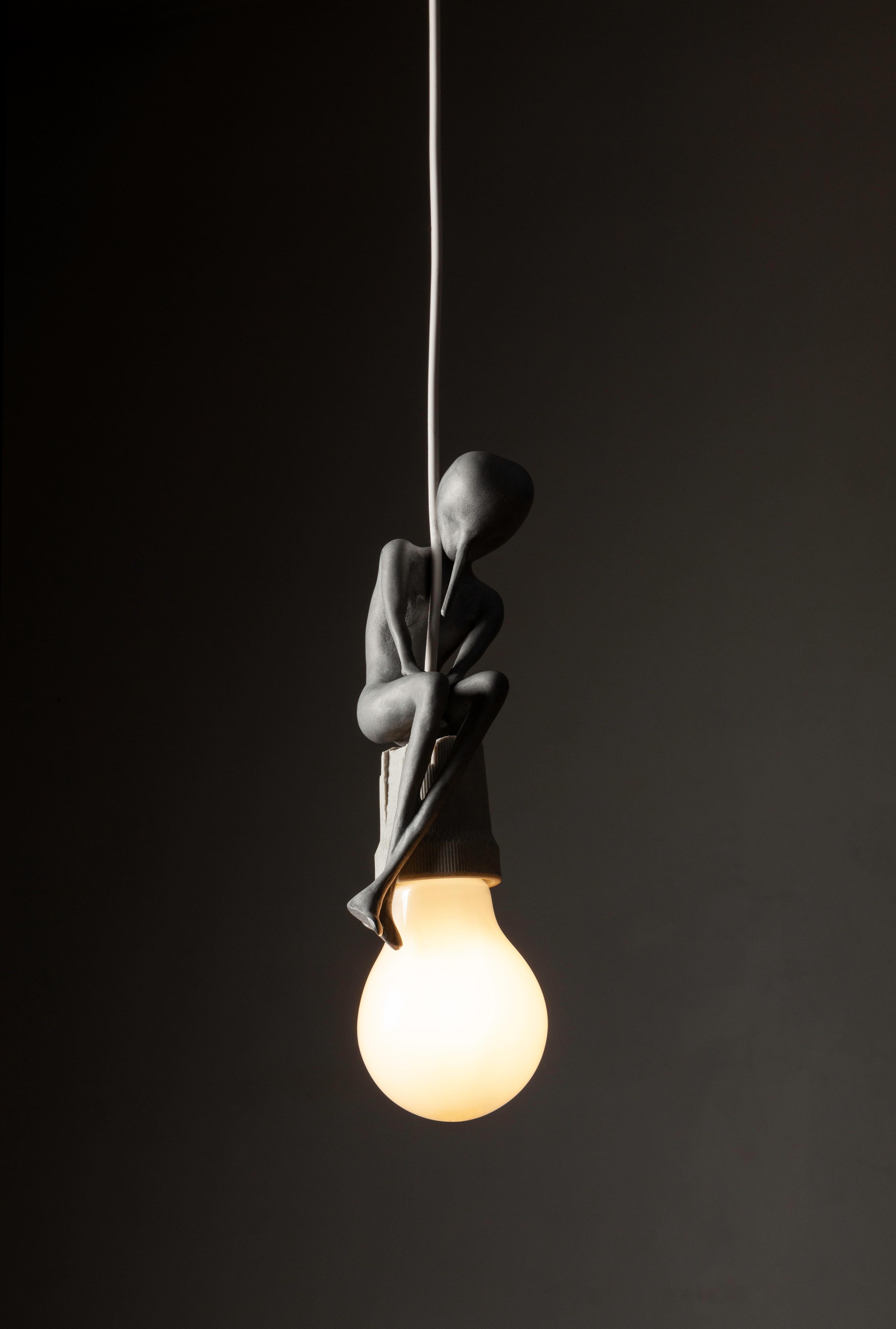 Lampada a sospensione realizzata in alluminio con fusione a cera persa per Dilmos Milano. Alex Pinna ha creato una collezione di tre lampade a sospensione chiamate Lampwick, Blue Fairy e Duo. Questo pezzo, Lampwick, è una piccola scultura seduta su