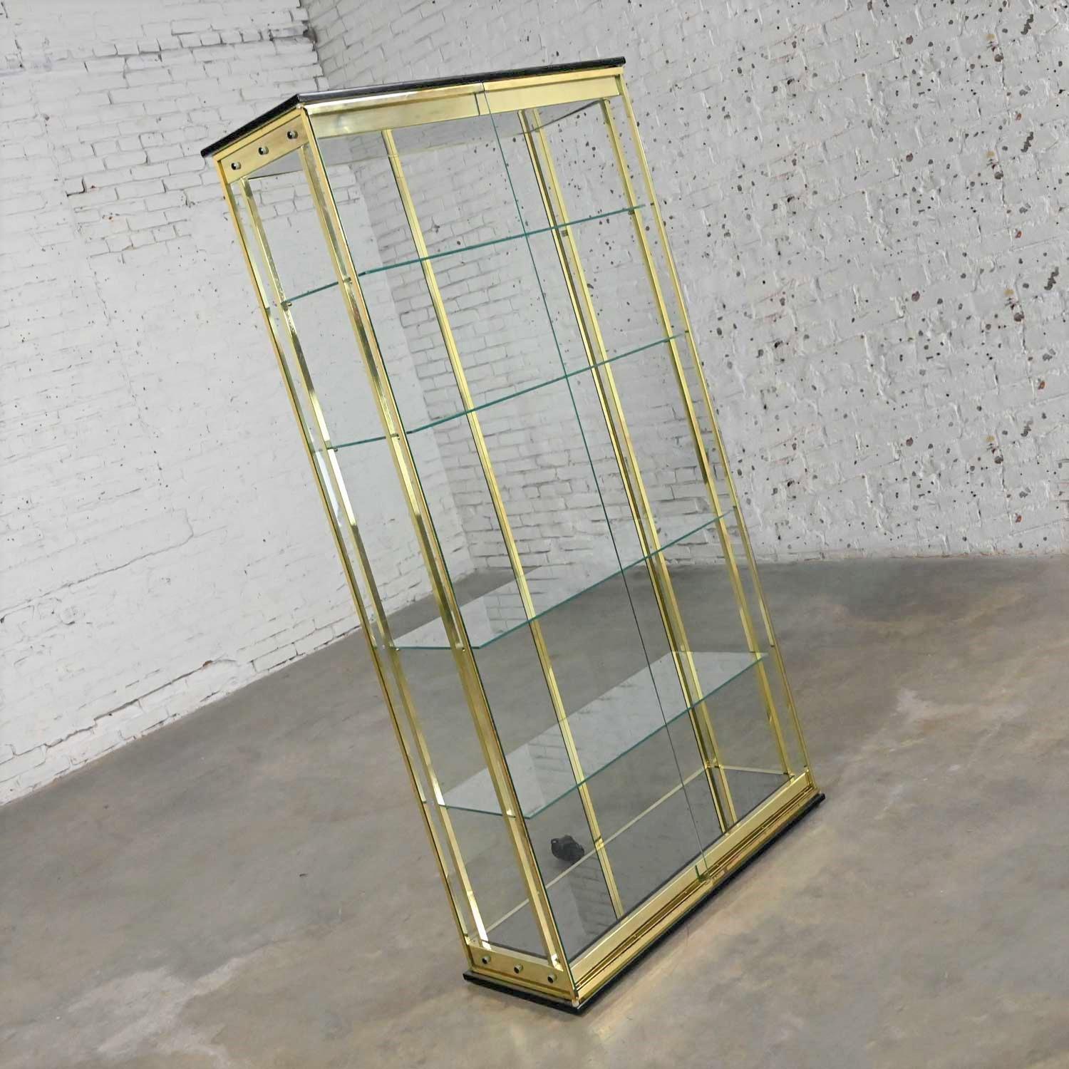 Gorgeous modern all glass lighted display cabinet with brass plated framework, mirrored bottom shelf, four glass shelves, and black painted bottom rim, crown, and stud details. Beautiful condition, keeping in mind that this is vintage and not new so