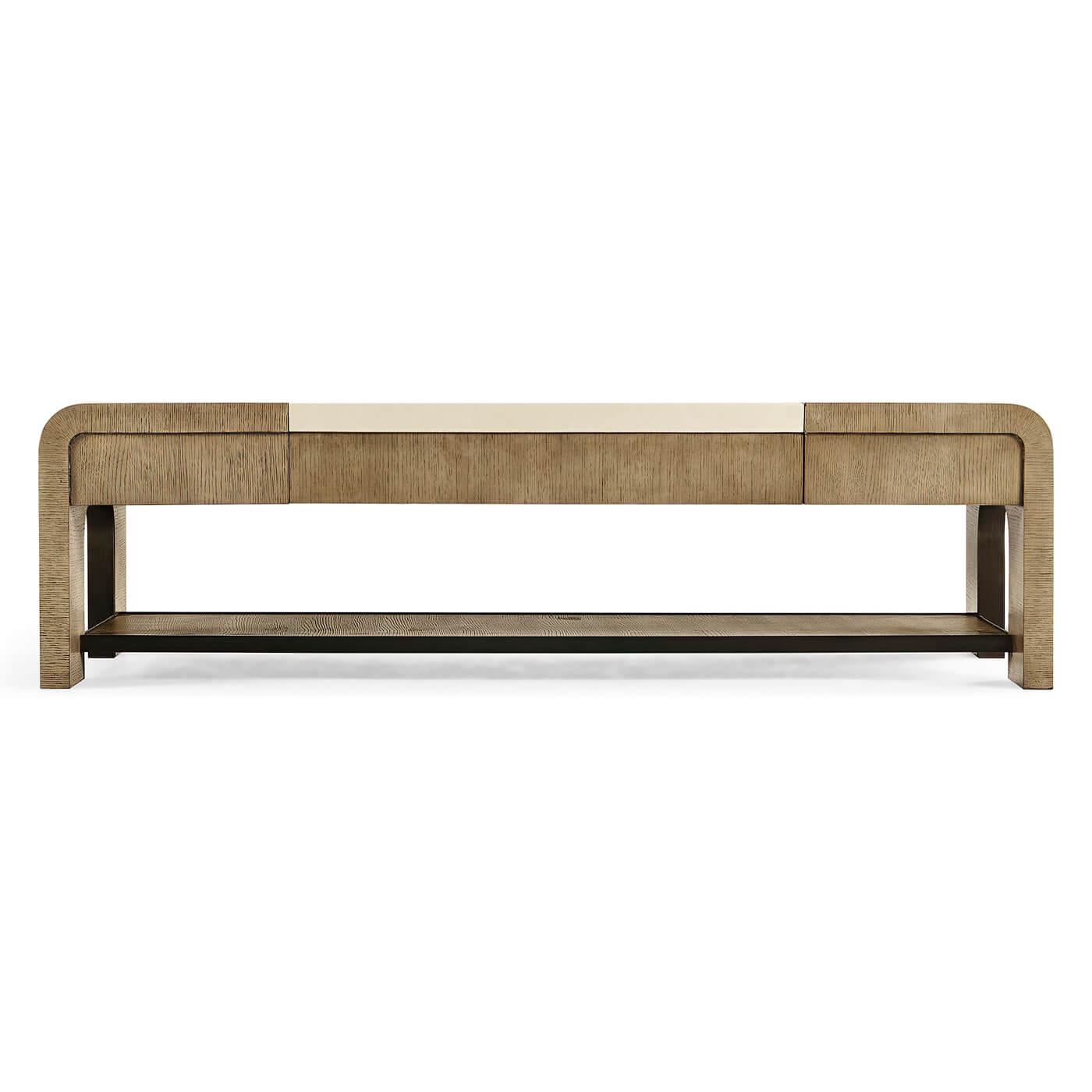 A modern coffee table, constructed from American white oak with a lightly textured ceruse finish. The table features rift cut veneers and a leather inlay. The shelf is framed in brass trim with a dark, rich patina and the table has a center