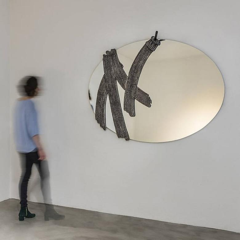 Miroir mural ovale en moulage au sable d'aluminium patiné pour Dilmos Milano. Reproduit le moment interrompu, la suspension dans l'espace et le temps qui se crée lorsqu'on fait un geste, même un geste simple comme un coup de pinceau.
Signé par le