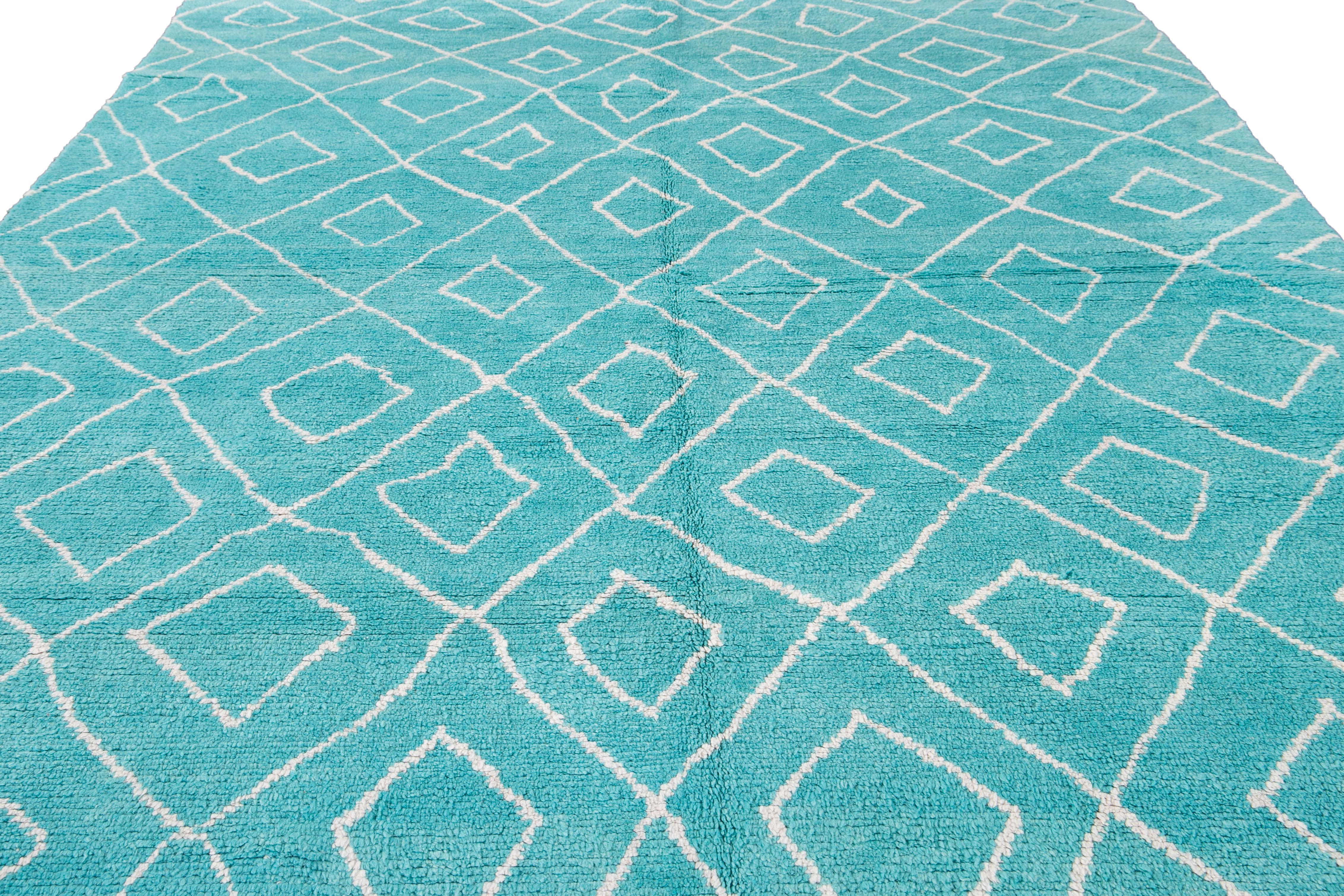 This exquisite hand-knotted wool rug highlights a mesmerizing Moroccan pattern, predominantly in an elegant ivory hue, which beautifully contrasts against a captivating background in aqua. The visually stunning Tribal design exudes a sense of