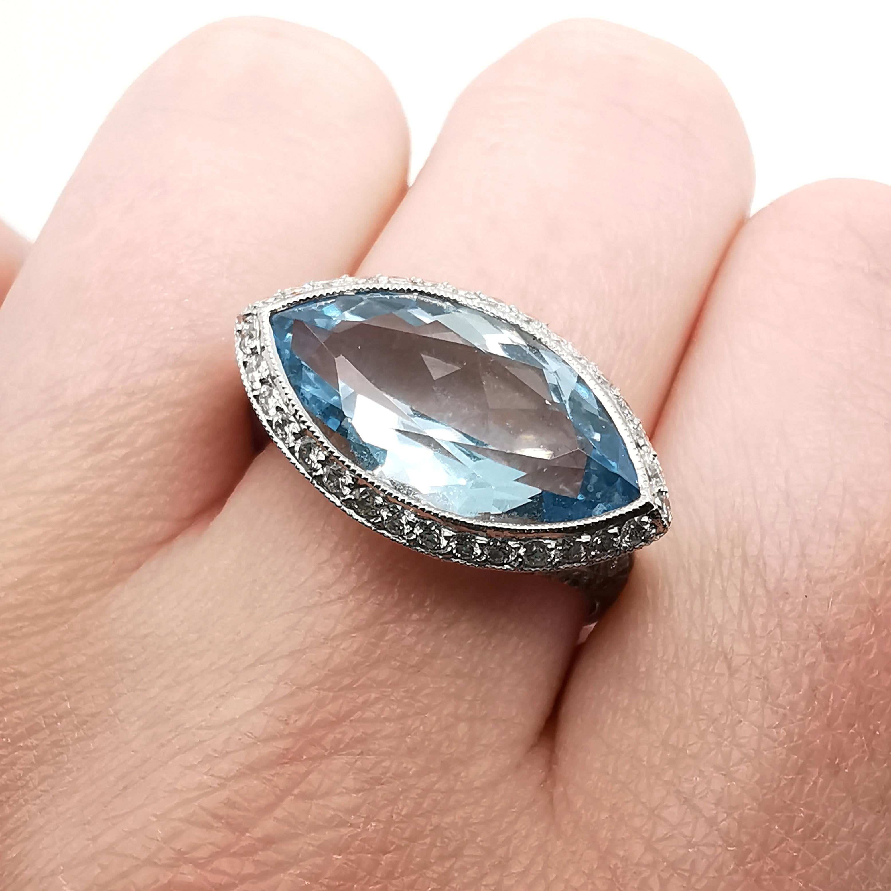 A modern aquamarine and diamond ring, with a marquise-cut aquamarine, weighing an estimated 4.69ct, in a millegrain edged rub over setting, with a grain set surround of round brilliant-cut diamonds, with decorative, round brilliant-cut diamond set