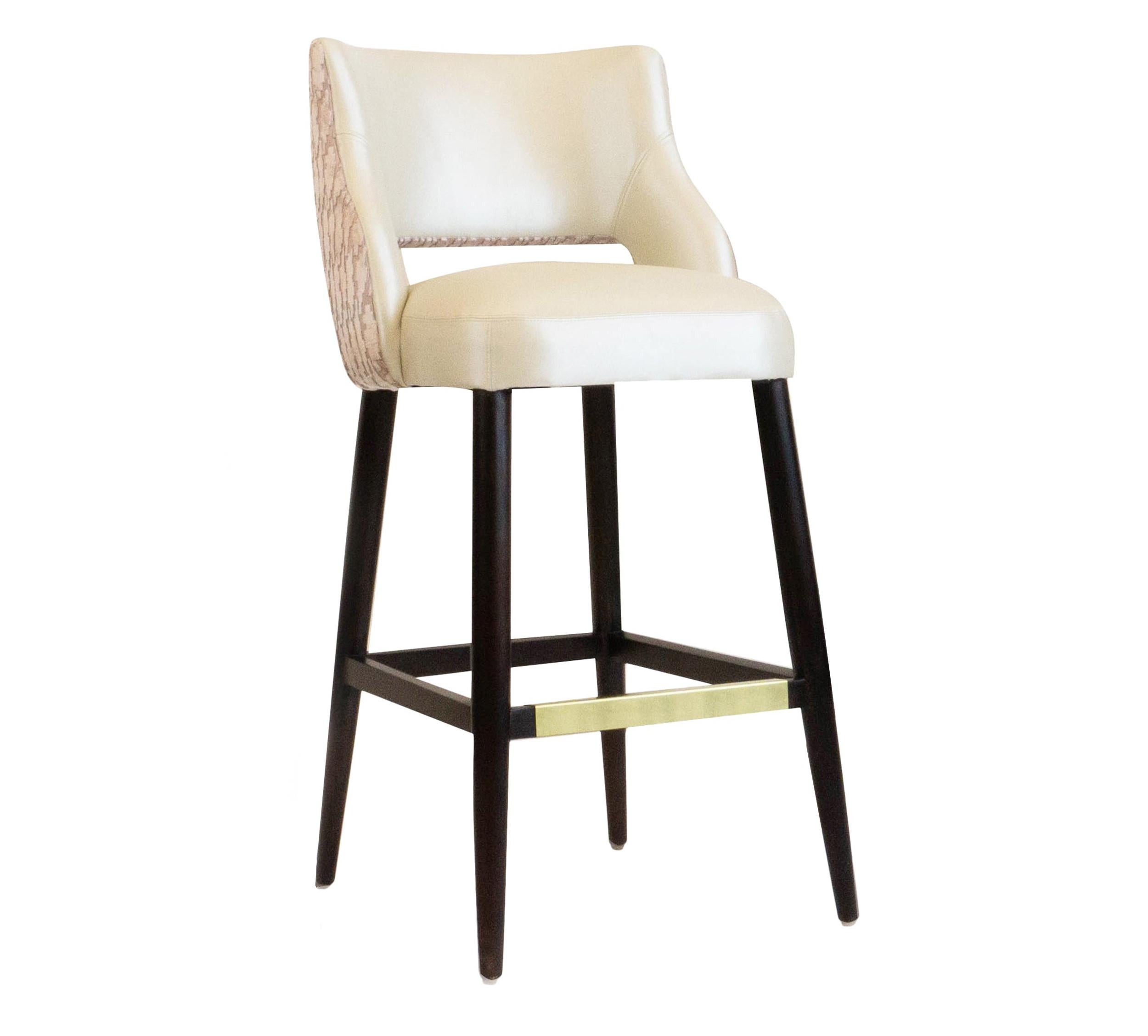 This armless bar or counter stool features a curvy and relaxed backrest. Upholstered in a shimmering vinyl with contrasting cut velvet on the back; the stool also features a brass kick. The bar stools are built to order and customization is