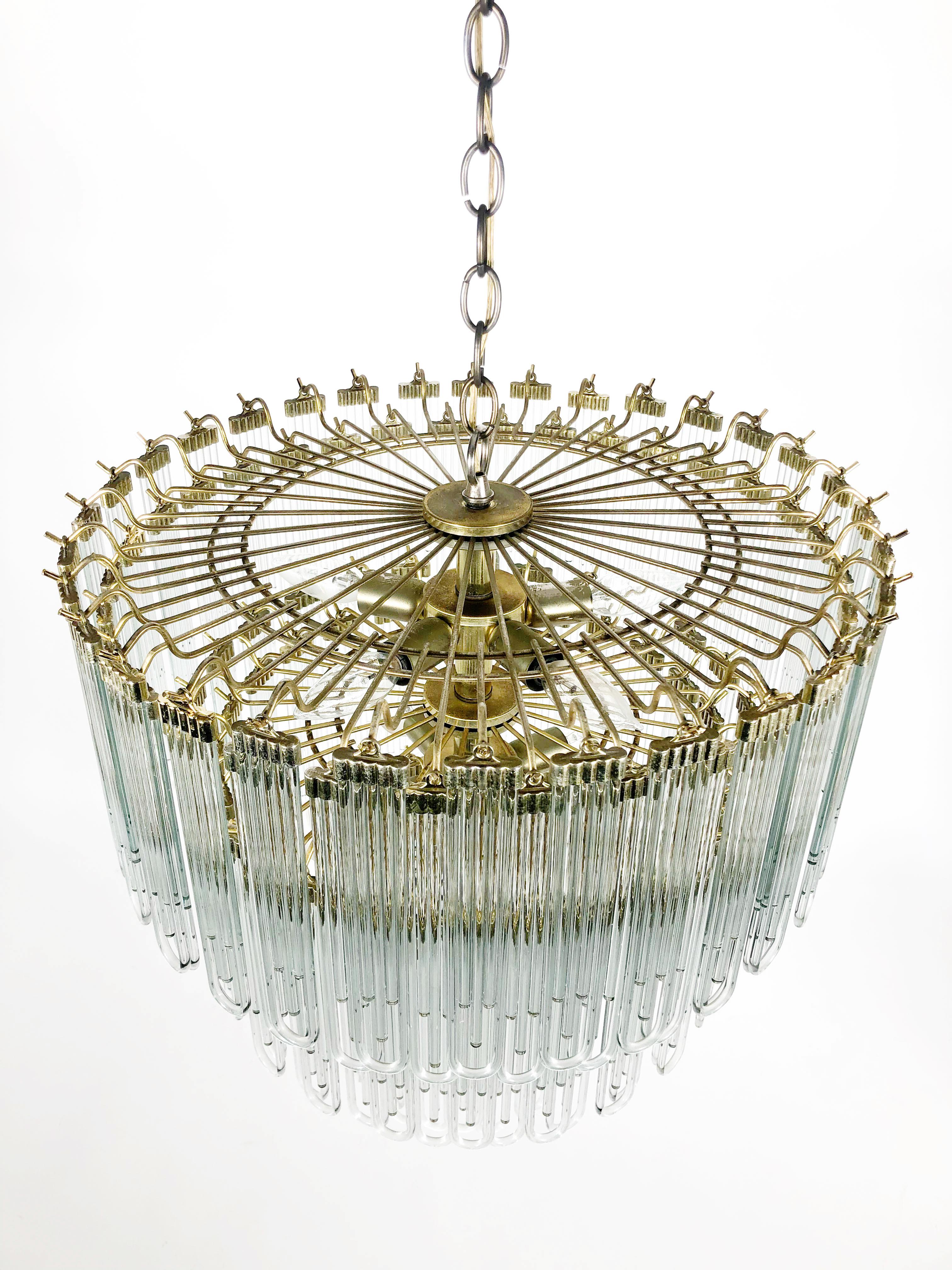 Stunning and unusual Art Deco inspired chandelier. The three tiered chandelier features unique tubular arched glass pendants, a gold plated frame and 10 candelabra sockets: 5 at the top, 4 in the middle and 1 center down light.
A box of