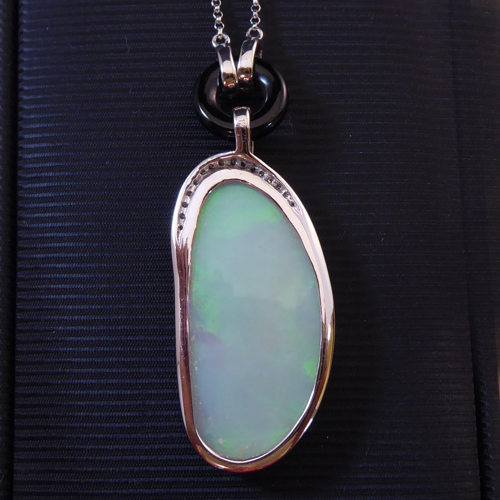 A modern opal and diamond pendant crafted in the Art Deco style.  Set with an oval cabochon opal with a diamond set border to the top half and suspending from a diamond set loop to a black onyx ring with two diamond set collars which are fitted in