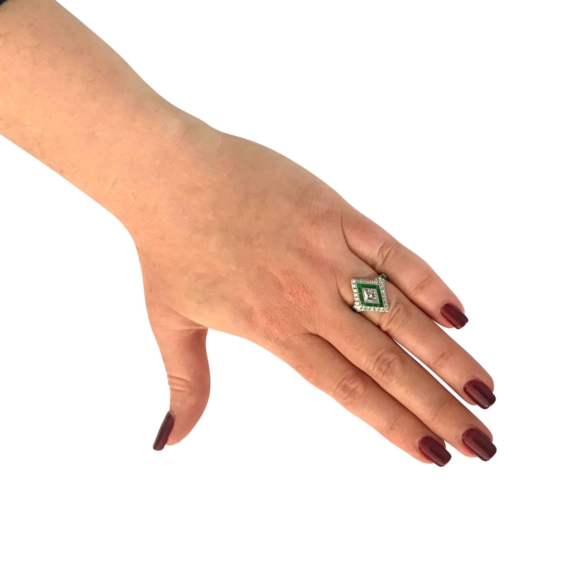 Art Deco inspired ring featuring an Antique rombus cut diamond weighing .85 carat G-H color, VS-SI clarity, set in platinum and framed with milgrain. The diamond rests on a bed of 12 vivid green custom cut emeralds, weighing approximately 1 carat