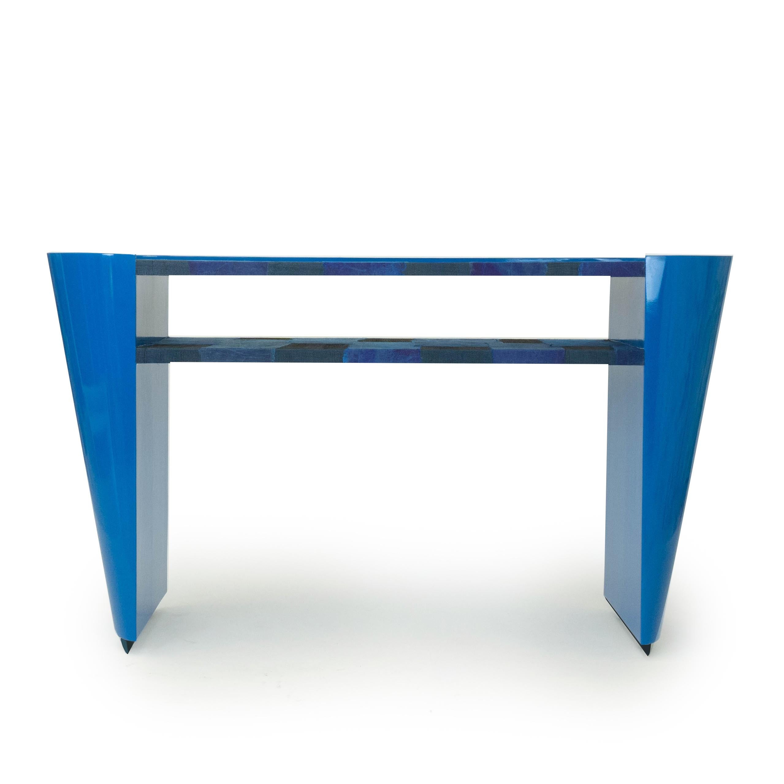 Our new modern Art Deco inspired console table is lacquered in laguna and marine blue. The table features a shelf and top covered in handmade woven raffias and pieces of paper. This piece is made with maple wood and designed with tapered, rounded