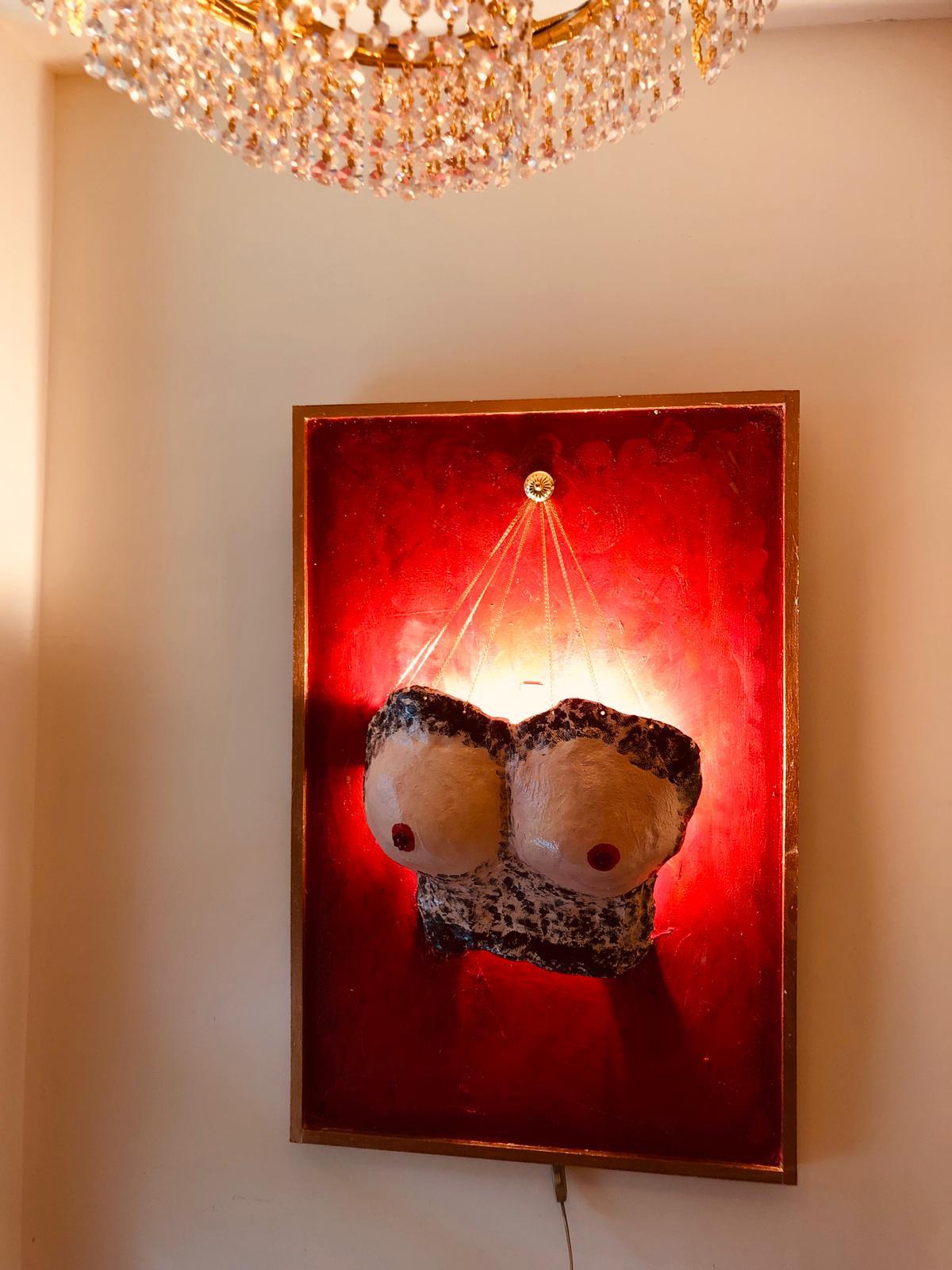 This is a unique piece from the 'Naked Breasts' collection. Here you can see a painting where ceramic parts are attached. The ceramic is attached to 24-carat gold-plated chains that come together at the top. The image is illuminated with two lamps!