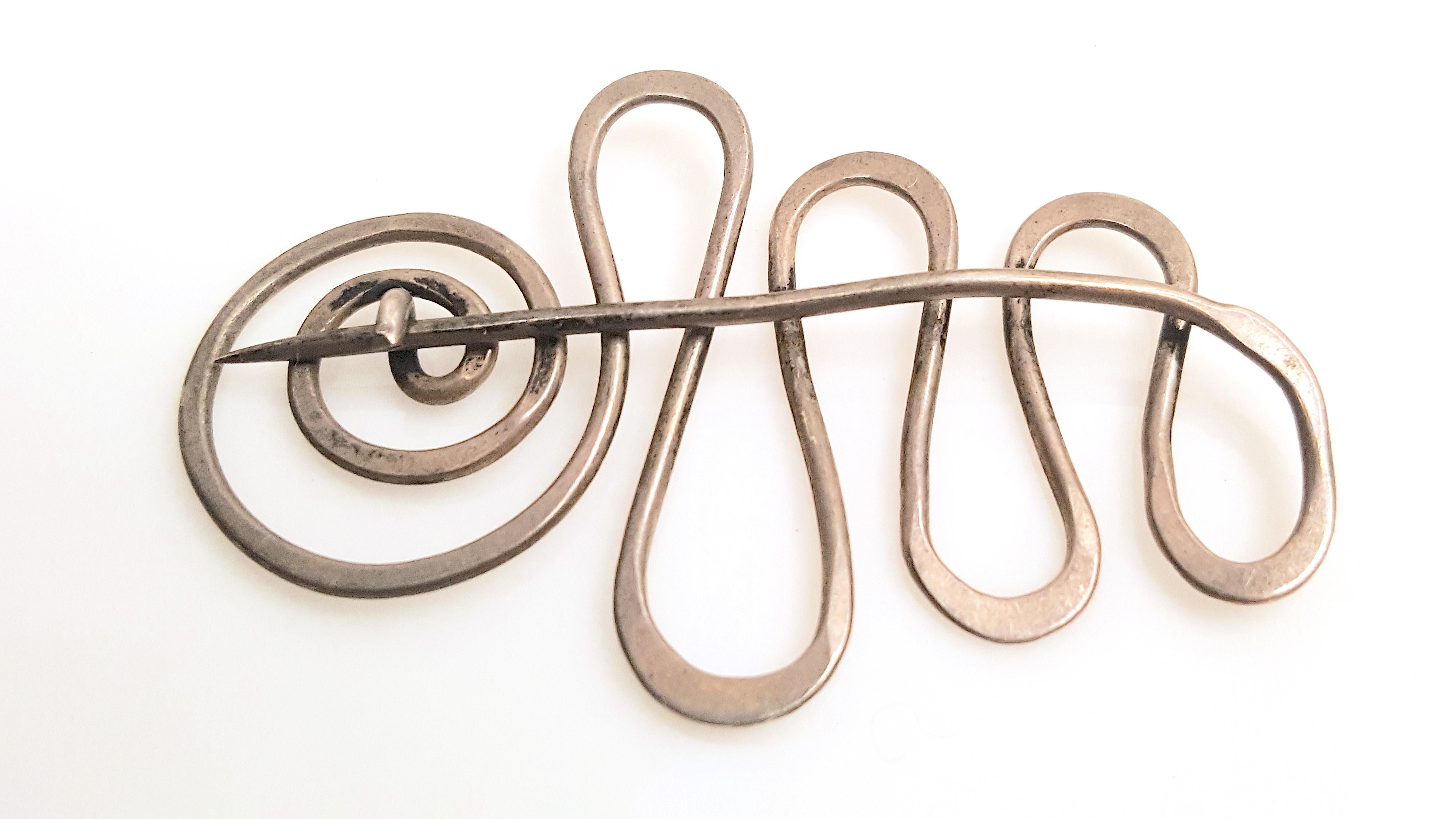 This modern mid-century abstract three-dimensional unsigned brooch is a single hand-hammered sterling-silver wire that was shaped by an artist into an undulating squiggle that ends in a spiral, which forms a c-clasp for self-closure while its other