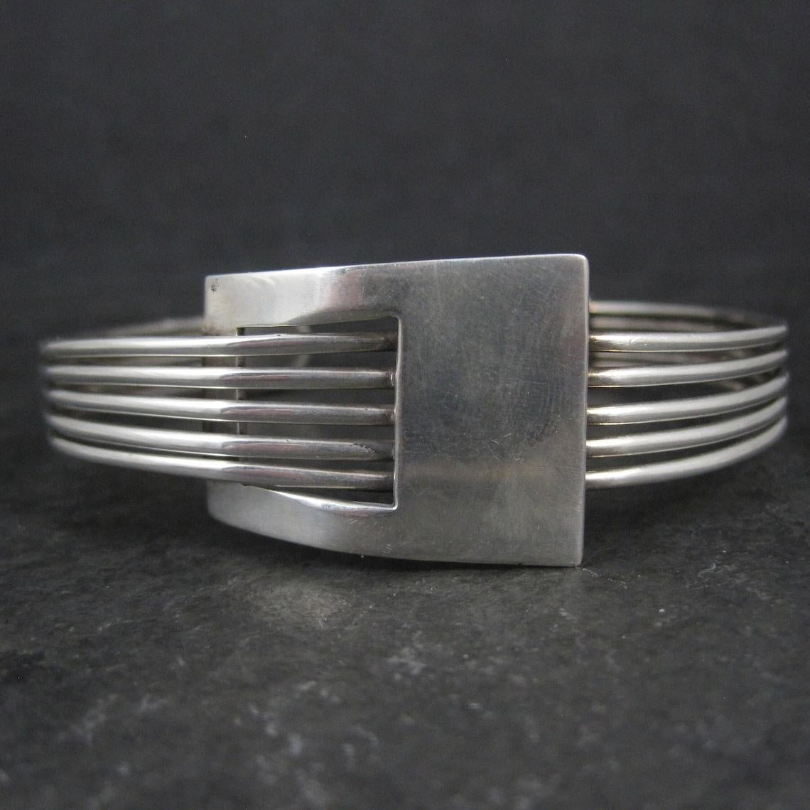 This gorgeous, mod style cuff bracelet is sterling silver.

The face of this cuff measures 7/8 of an inch at its widest point and tapers down to 3/8 of an inch.
It has an inner circumference of 7 inches, including the 1 inch gap.
Weight: 26.8