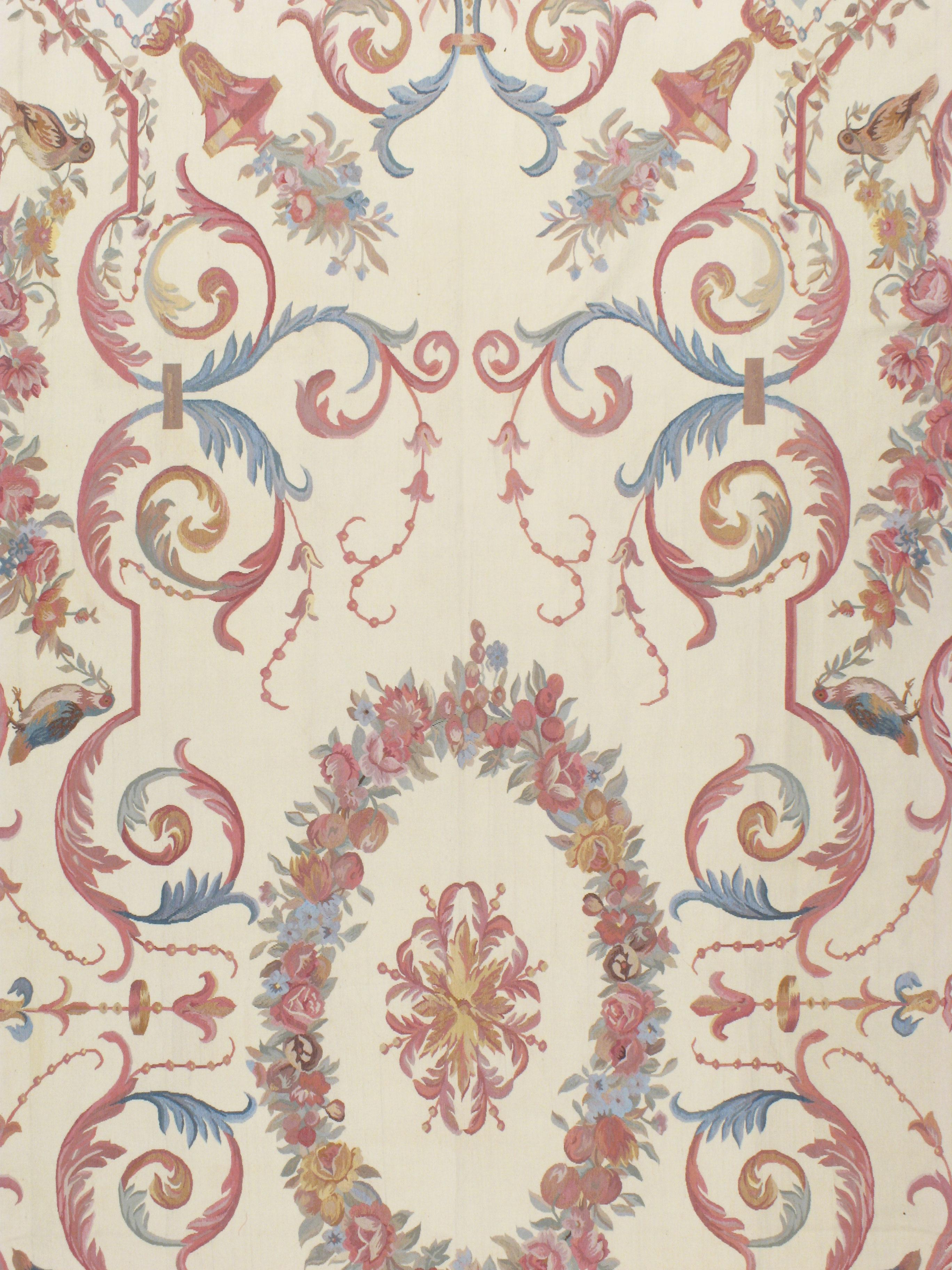Une reproduction contemporaine faite à la main de l'intemporel tapis français d'Aubusson dans le style de Louis XV. Le motif floral est composé de couleurs telles que le rose, le bleu et le gris, sur un fond ivoire. Grandeur dans la taille et