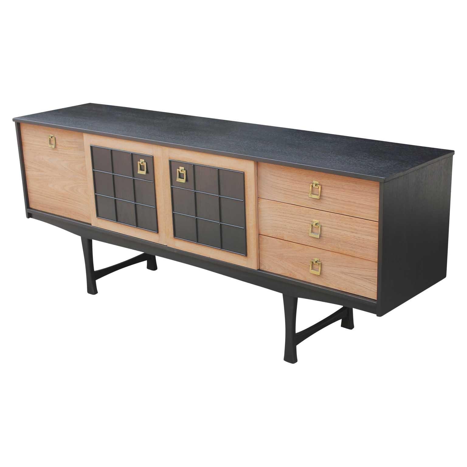 Modern credenza / sideboard freshly refinished in a lovely two-tone manner in the style of Baker Furniture with brass hardware. This piece features two cabinet spaces on the left and three drawers on the right.
