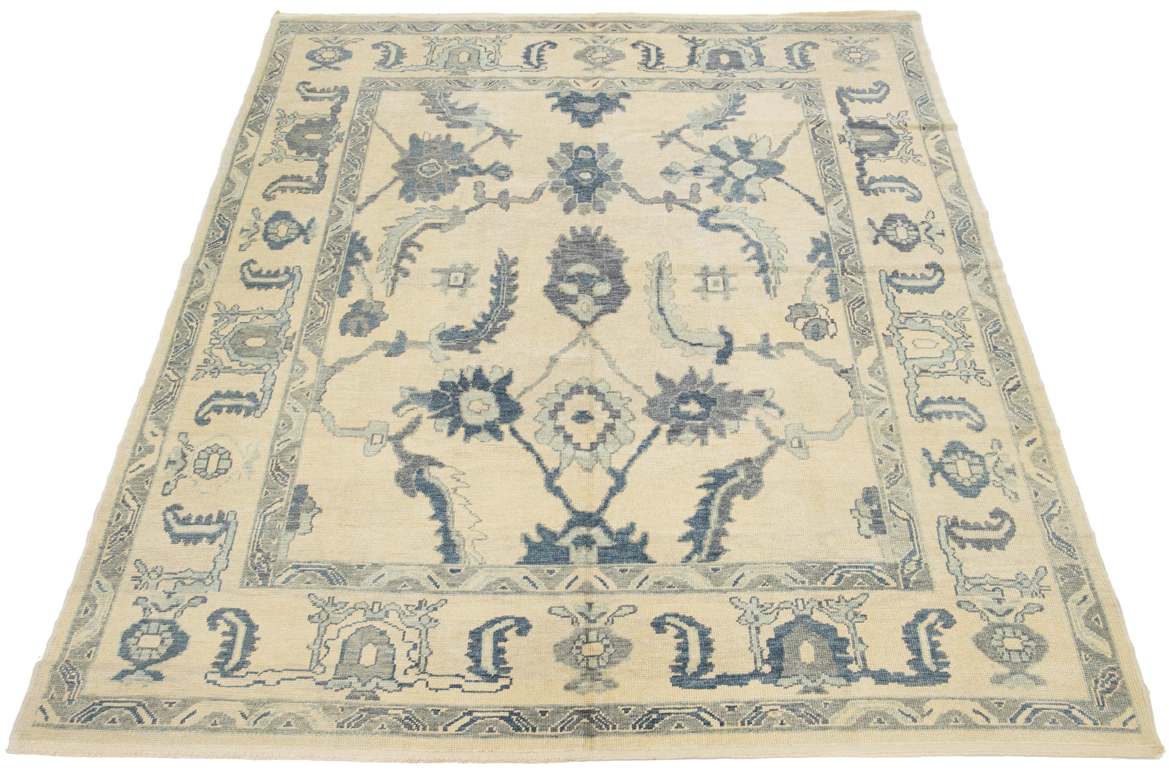 Beautiful modern Oushak hand-knotted wool rug with a beige field. This Oushak rug has blue and gray accents all over a gorgeous geometric floral design.

This rug measures 9'2