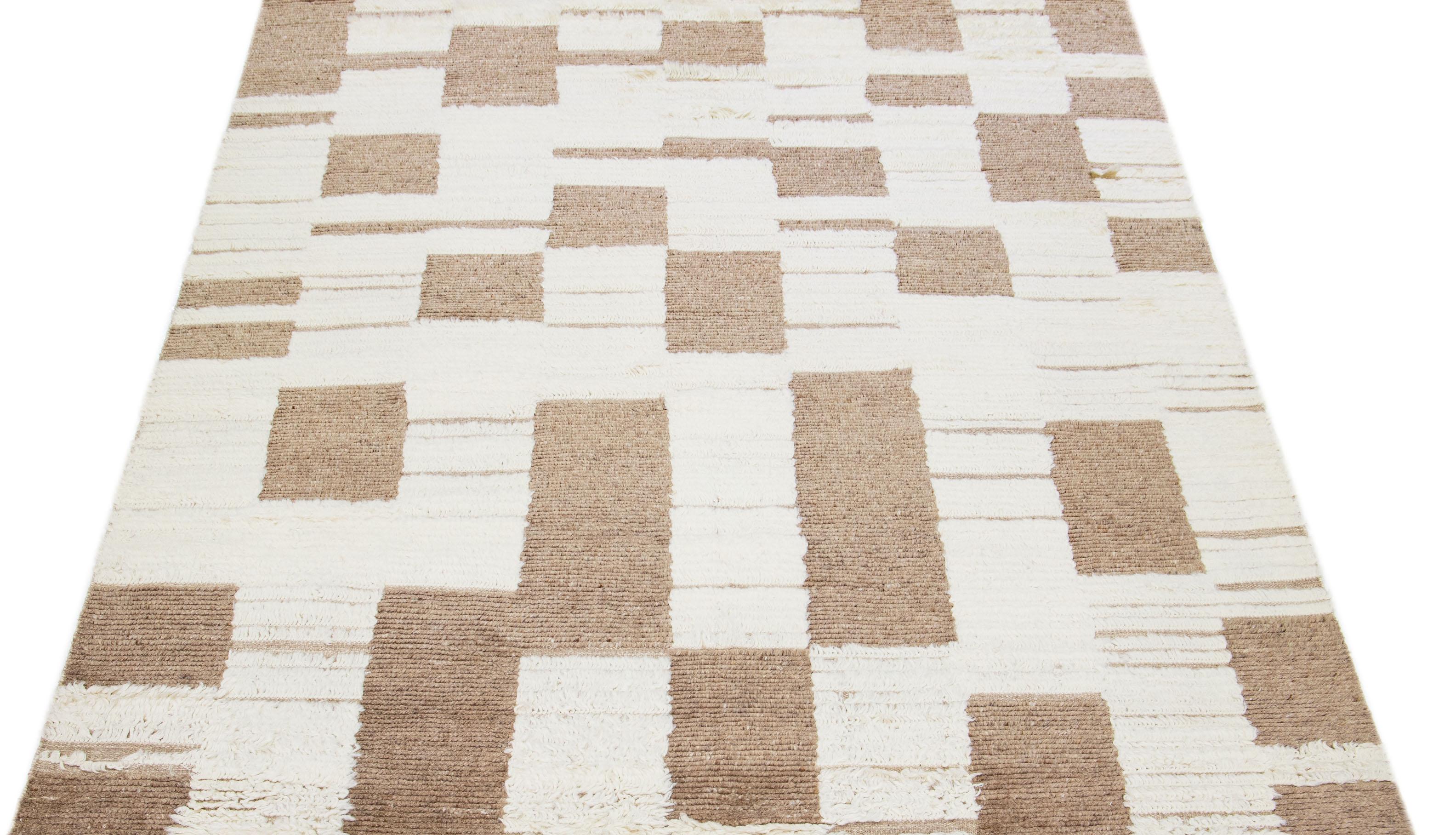 Dieser sorgfältig gearbeitete Wollteppich zeigt ein marokkanisches Muster, das in verschiedenen Brauntönen gewebt ist. Sein fesselndes elfenbeinfarbenes Gewebe bildet einen atemberaubenden Kontrast, der die Schönheit des Teppichs insgesamt