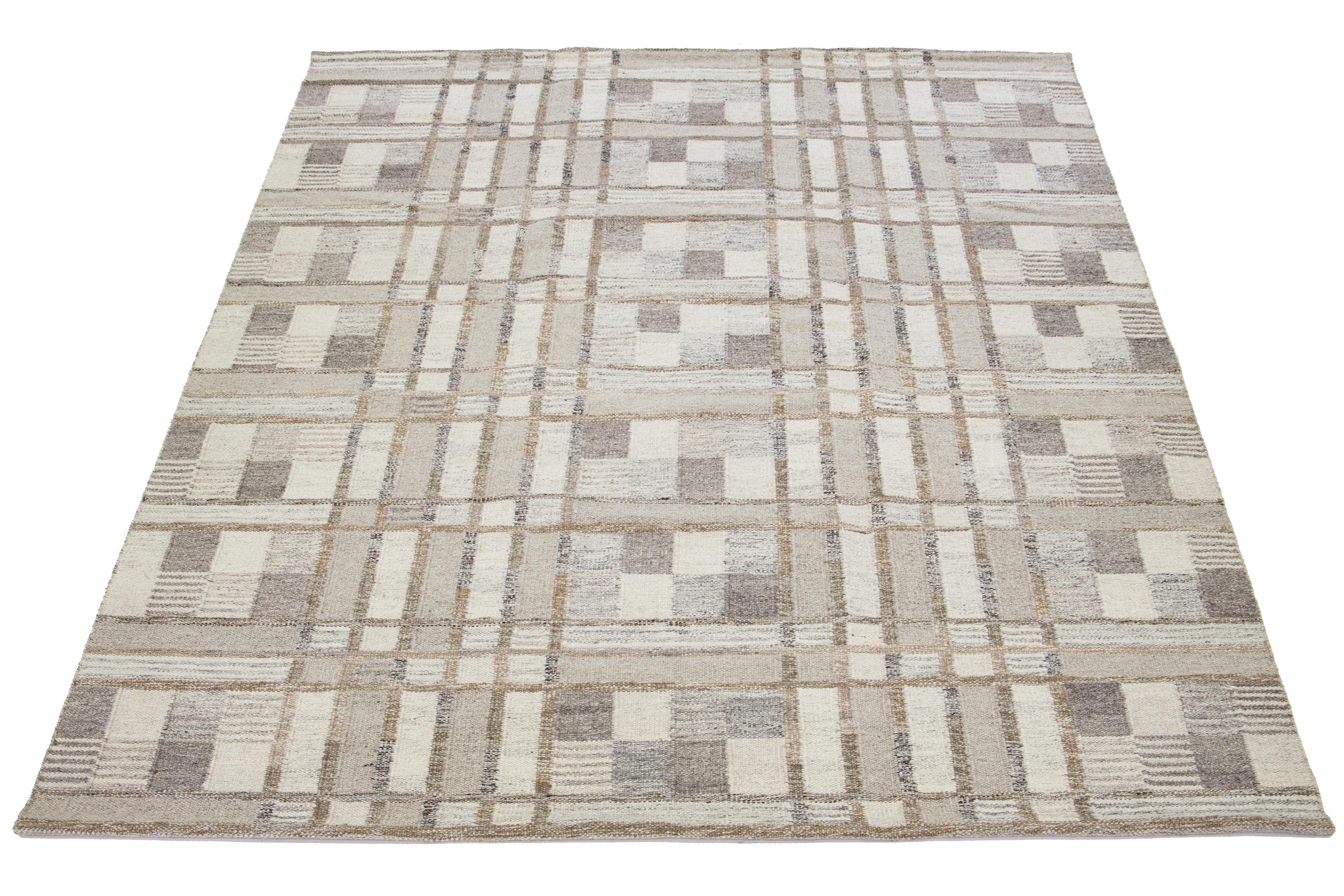 This flatweave rug features a chic contemporary Swedish design with a beige field color. It has a geometric pattern throughout the rug in ivory, gray, and brown shades.

 This rug measures 9'1