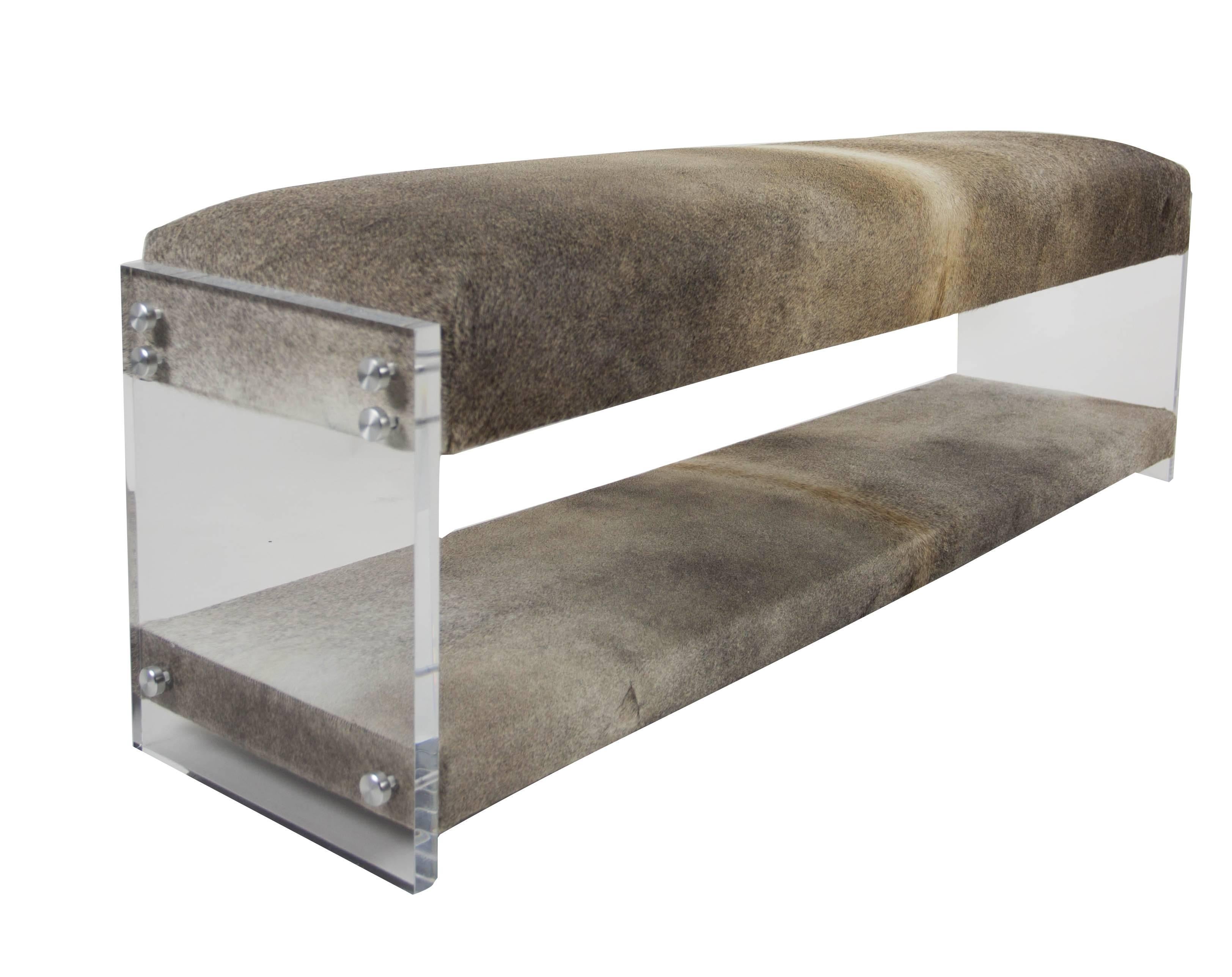 Our Hide and Sleek Bench is an accent bench with a modern design. The bench features a high density foam seat cushion upholstered in cowhide with a bottom tier for storage. Clear acrylic sides serve as legs. This piece is built to order with custom