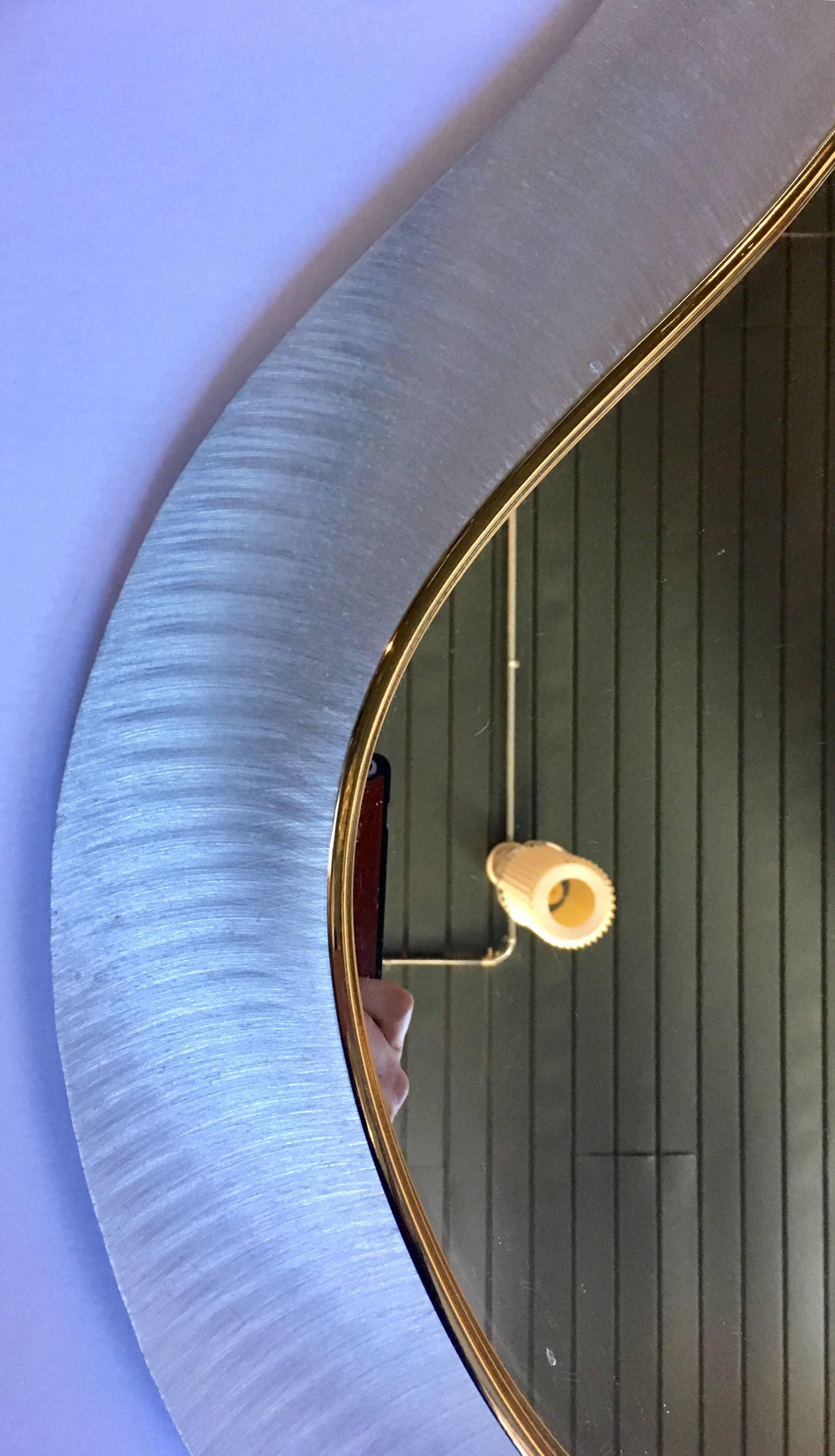 Modern abstract form wall mirror featuring a reflective moire-like brushed steel laminate sheet with gold band detailing.