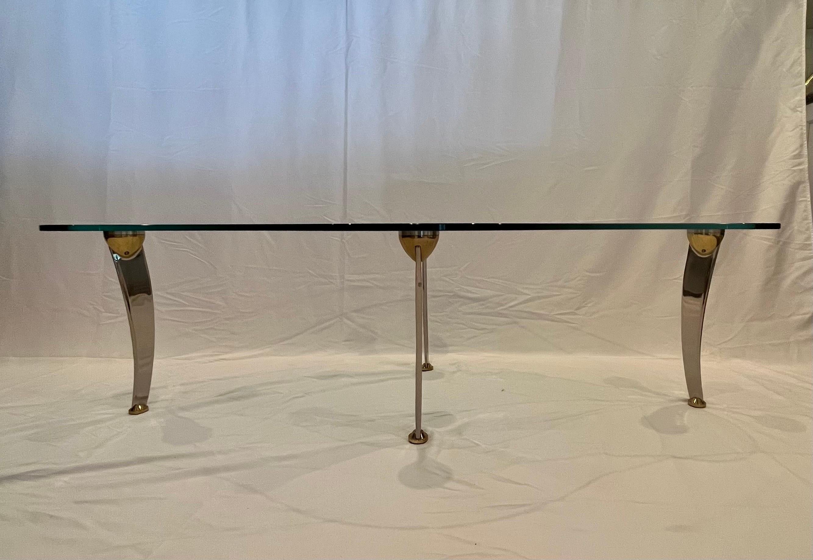 Table basse unique en verre de forme irrégulière avec pieds en chrome et laiton. Fabuleux effet de flottement. Pieds chromés évasés ou serpentins avec un lourd support conique en laiton et des pieds plafonnés en laiton. 
En bordure de route vers