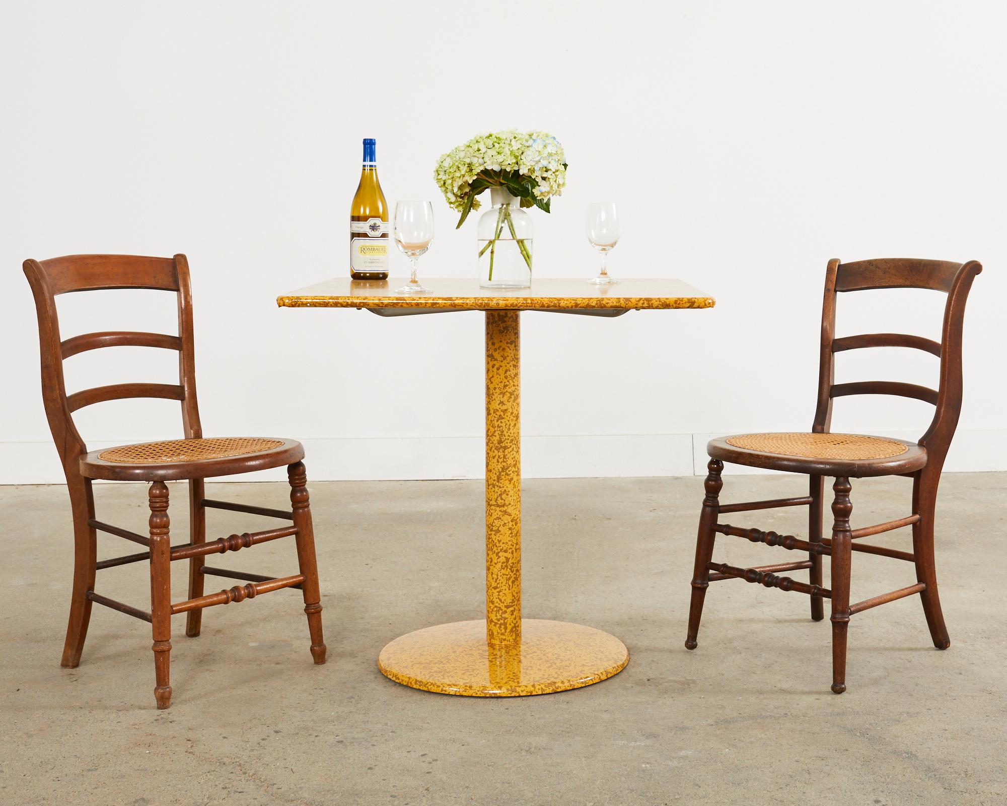 Contemporary modern steel bistro or cafe style dining table lacquer spreckled by artist Ira Yeager (American 1938-2022). The pedestal table has a steel frame and a square top with round edges. The table has brown specks over a dramatic mustard