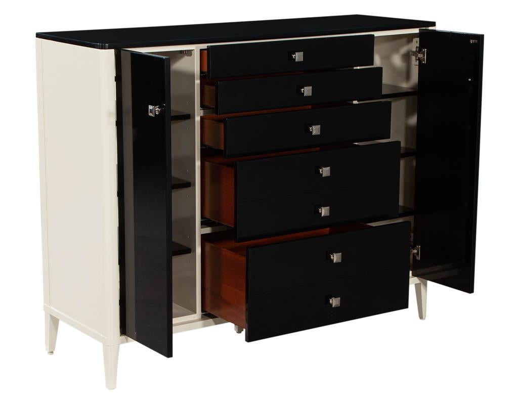 Modern black and white wardrobe cabinet chest. Featuring sleek curved corners and legs. Lacquered in a 2-tone decorator white and black. Completed with polished stainless-steel hardware and black felted drawers. Ample storage options within its 5