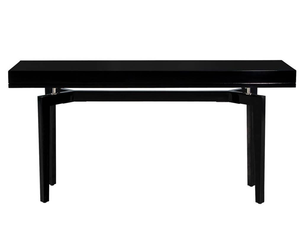 Modern Black Lacquered Console Table. America, circa 1970s. Masterfully restored in a high gloss black lacquered finish. Unique 1970s Mid-Century Modern design with stretcher base and beautiful stainless-steel accent supports. Price includes