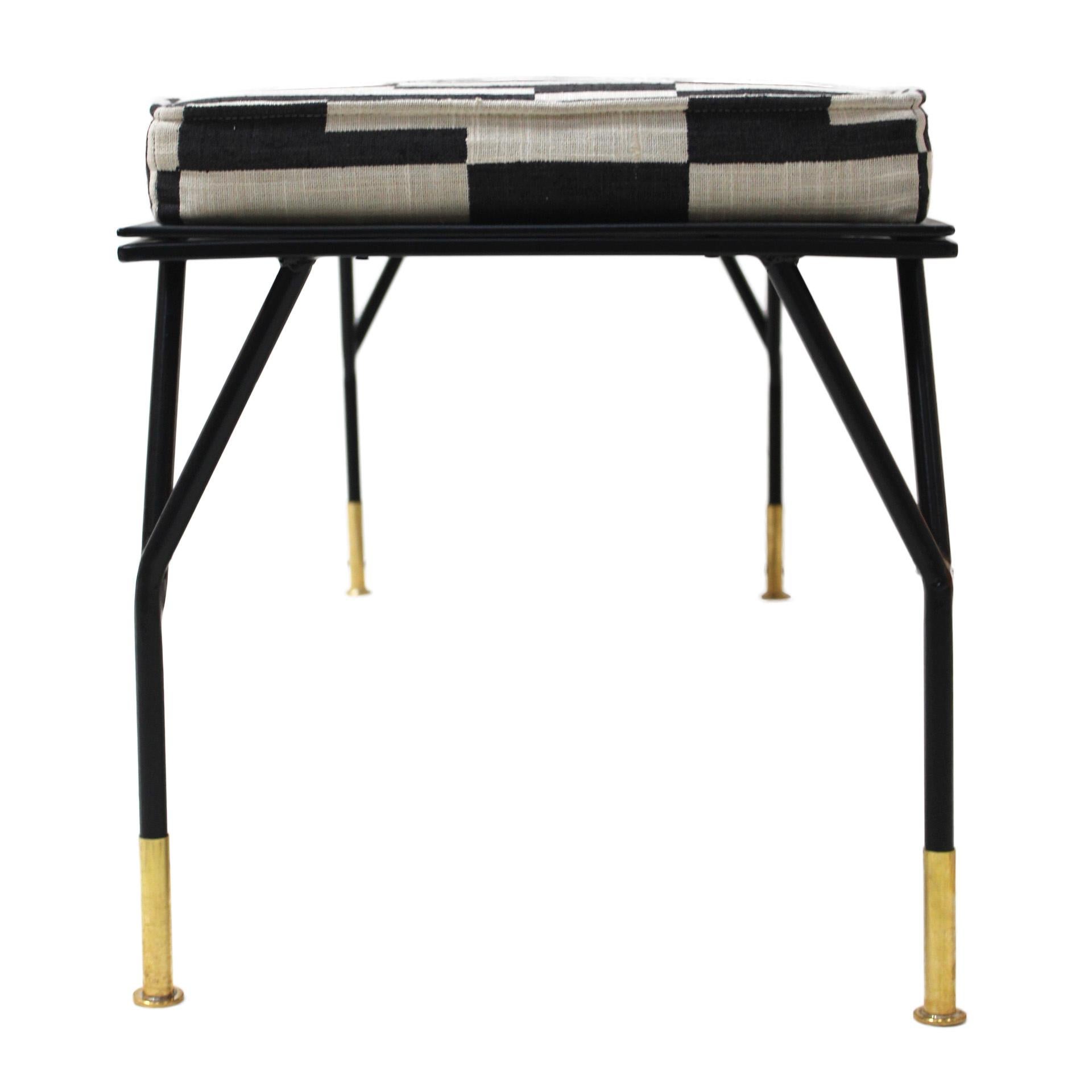 This footstool features a design inspired by Ico Parisi, crafted with a lacquered iron structure in black and brass-sleeved legs. It has been reupholstered in linen fabric with a stylish black and white rectangular print. Combining vintage elegance