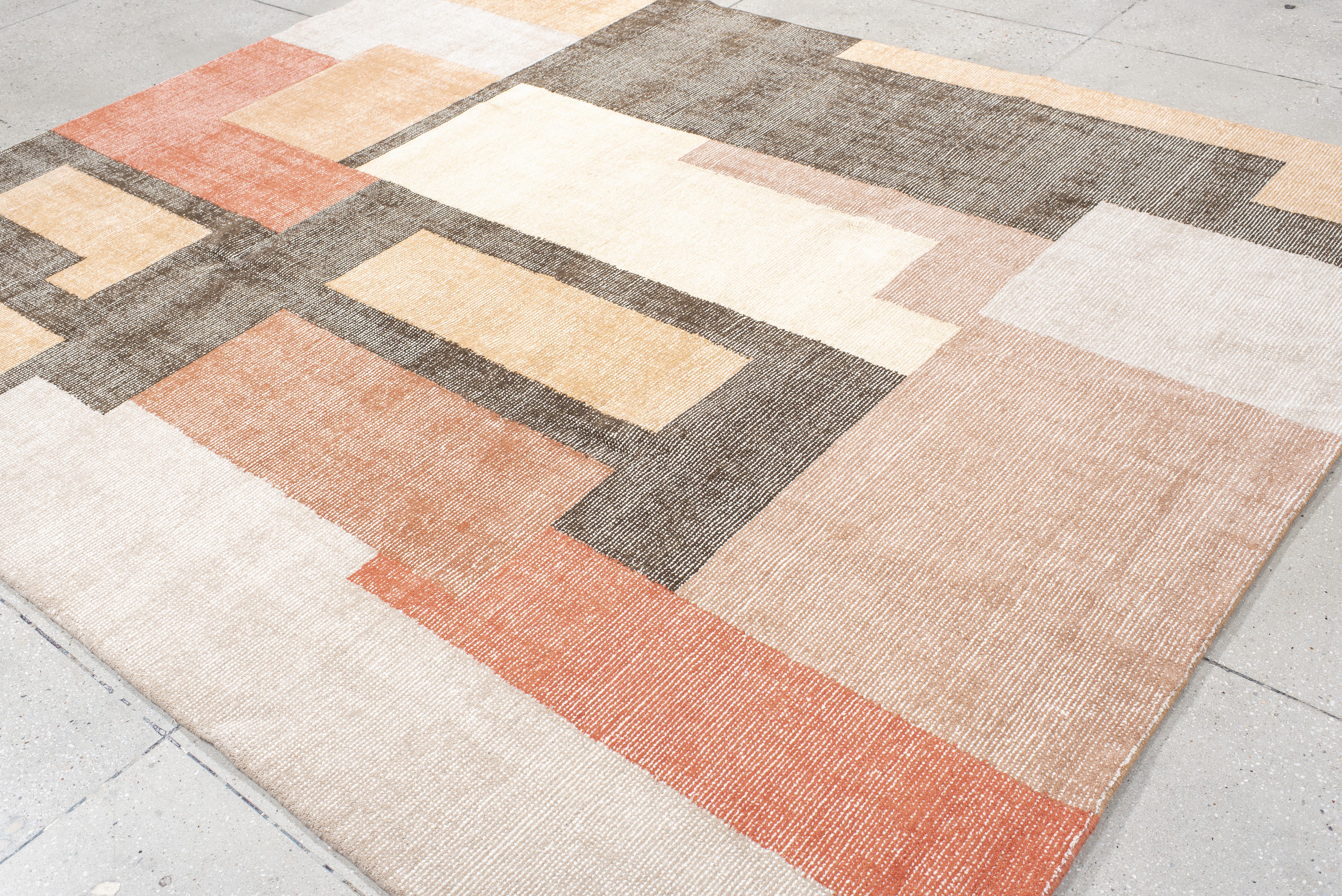 Ce tapis contemporain tissé à la main présente un jeu vibrant de formes rectangulaires dans les tons terracotta, pêche douce, ivoire et anthracite. La disposition dynamique des blocs donne une impression de rythme et d'énergie, tandis que les tons
